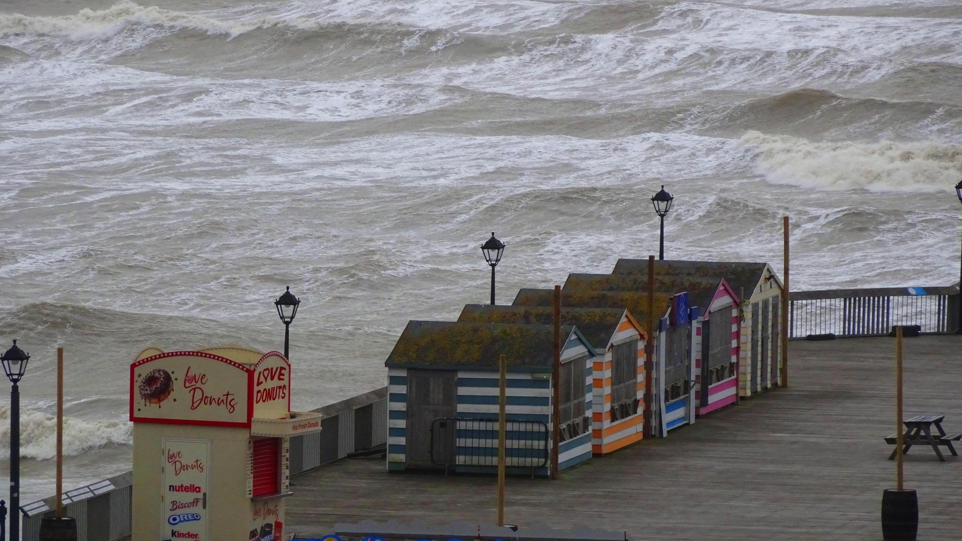 Beach huts on Hastings seafront during Storm Bert, grey, choppy sea seen in the background