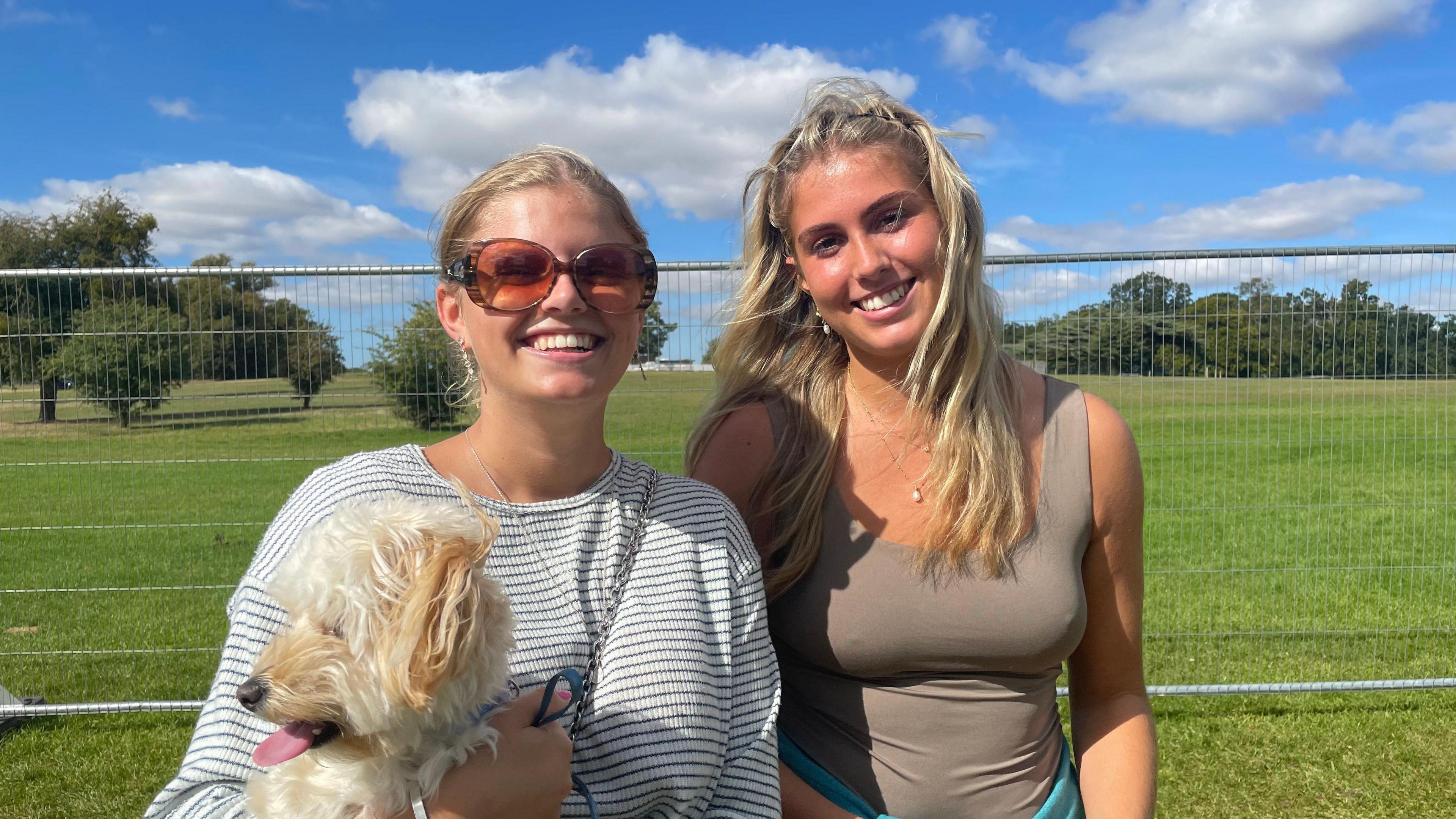 Two blonde haired women smiling, one with large sunglasses and holding a white dog