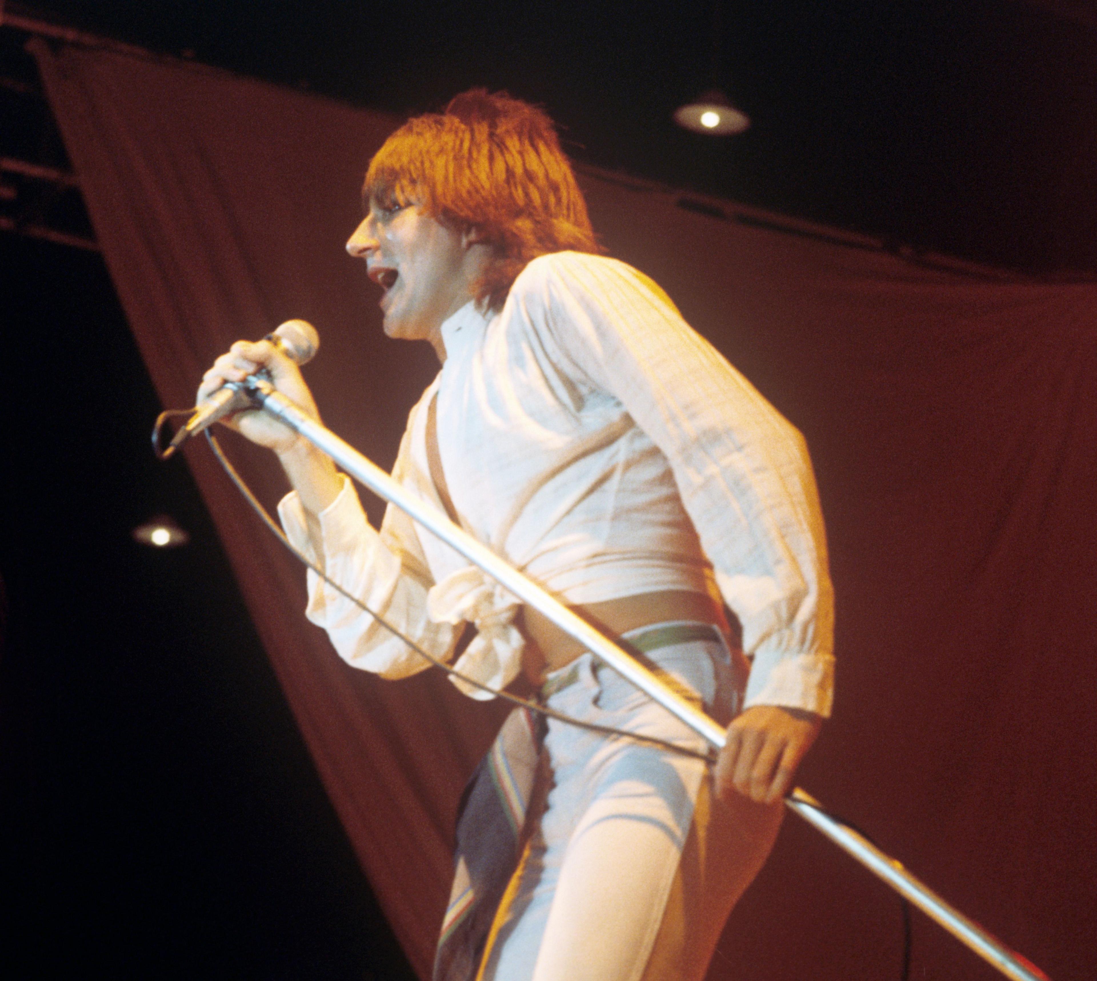 Rod Stewart holds a microphone stand and sings, in a picture taken in the 1970s