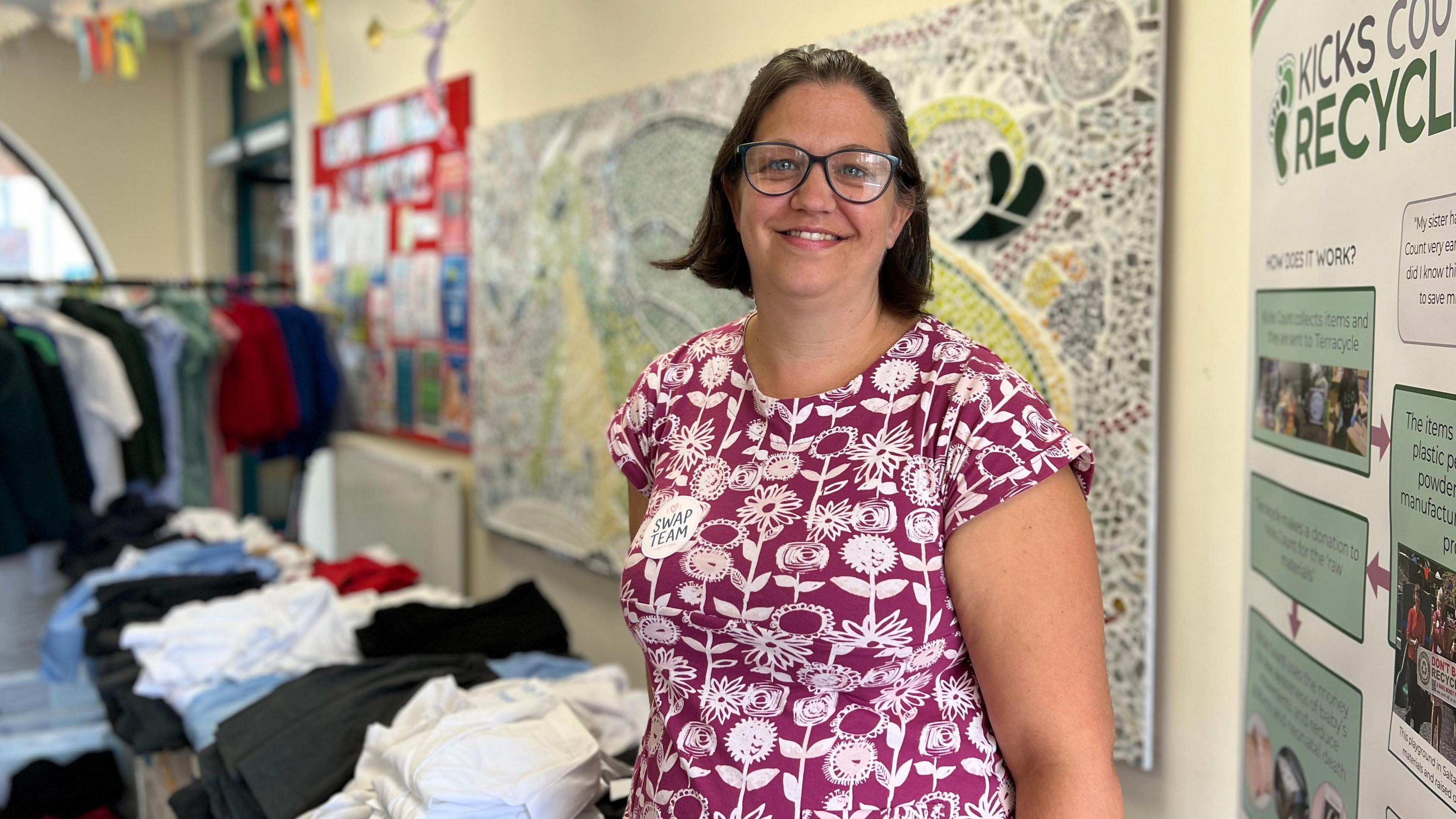 Bex smiling at the camera in front of a table filled with folded school uniform items.