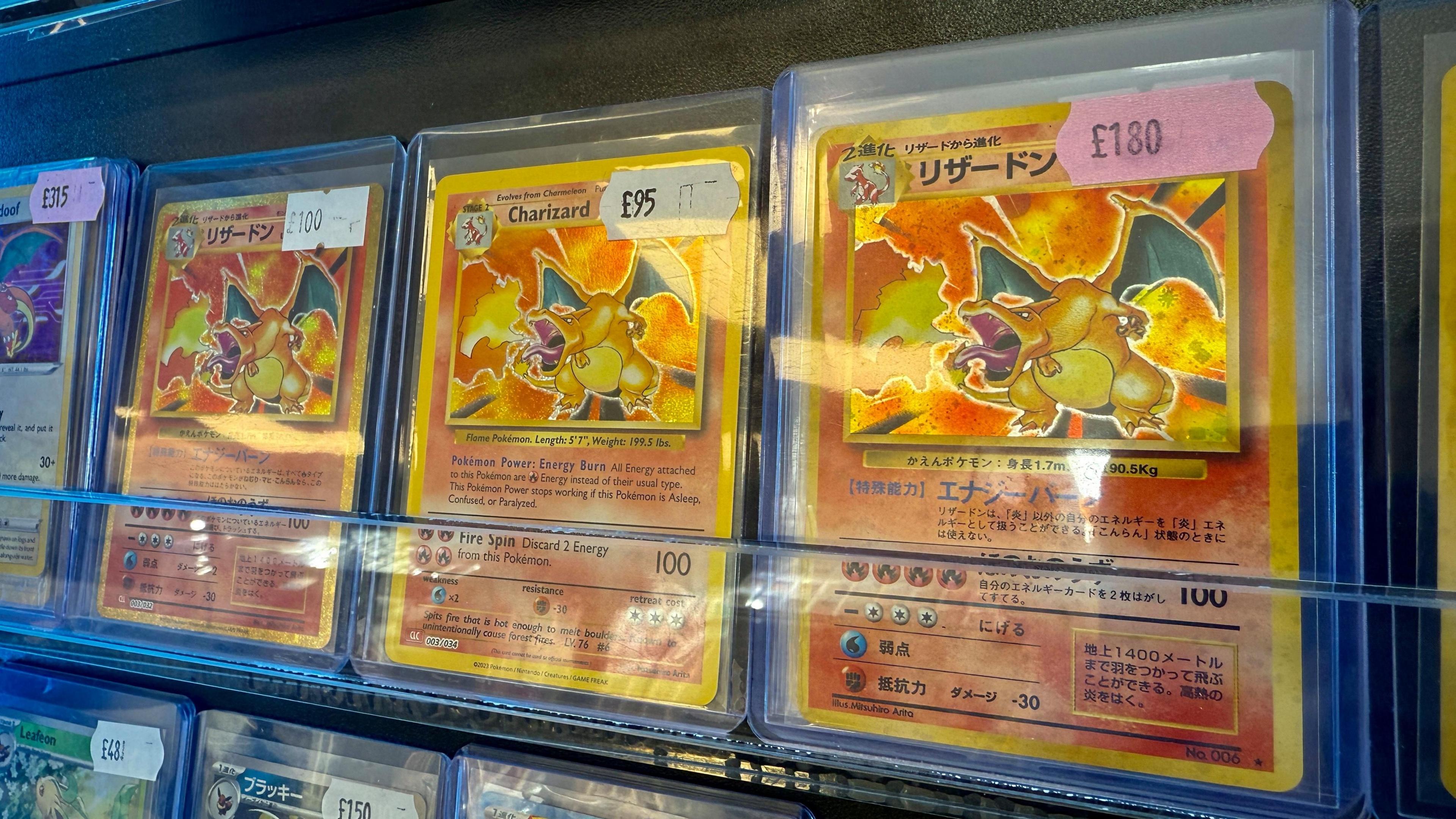 Three Charizard cards in plastic wallets are on display. All are holographic shiny cards, two are Japanese and have values attached of £180. An English card is worth £95.