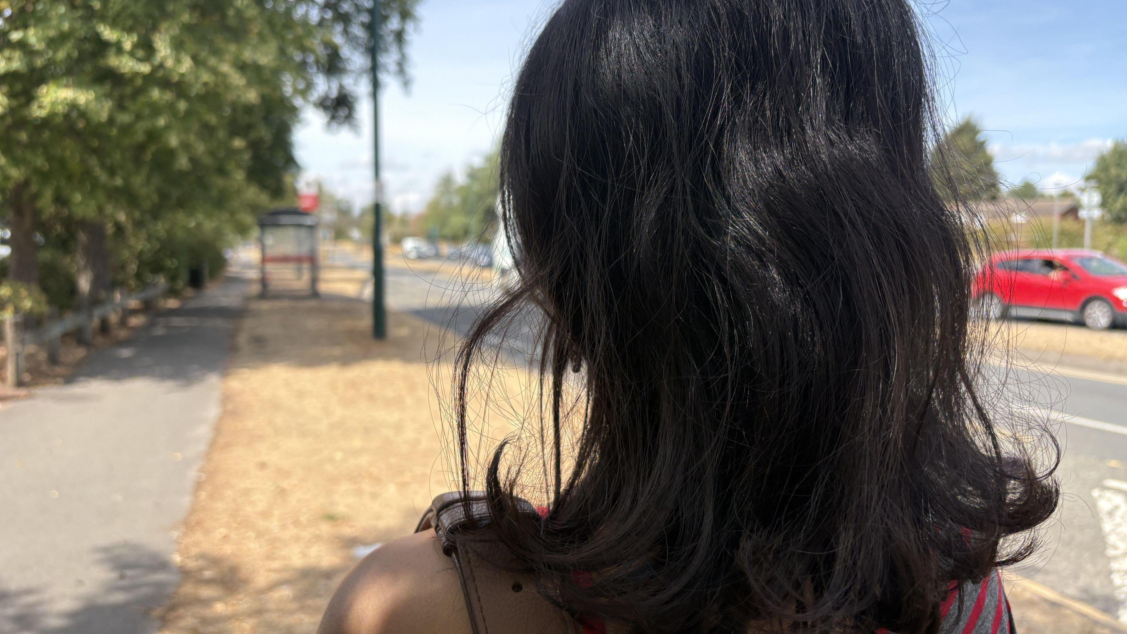 The back of an anonymous woman who has shoulder-length black hair. She is wearing a grey and red off-the-shoulder top