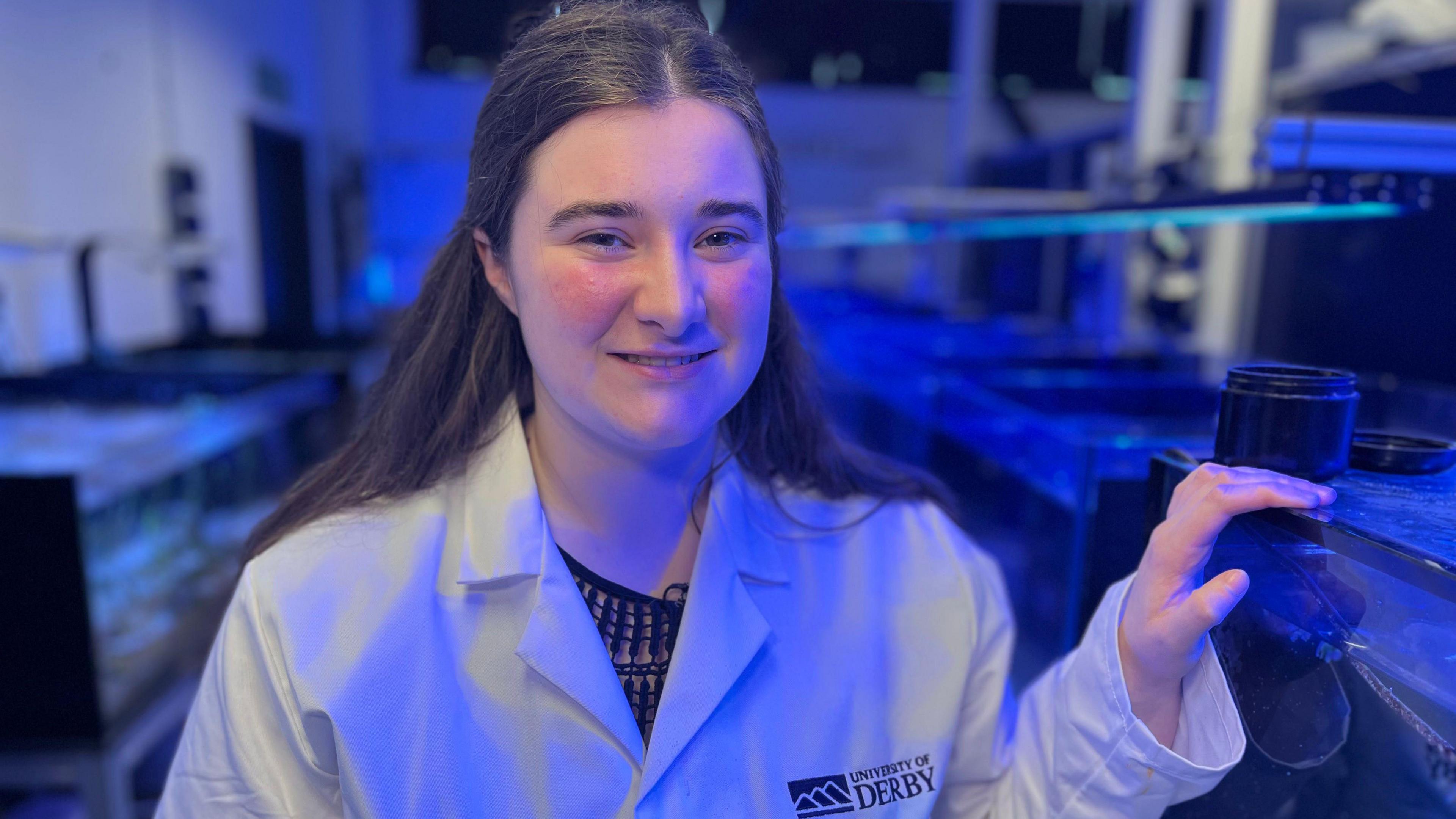 Triona Barker in a white lab coat stands beside her lab experiments