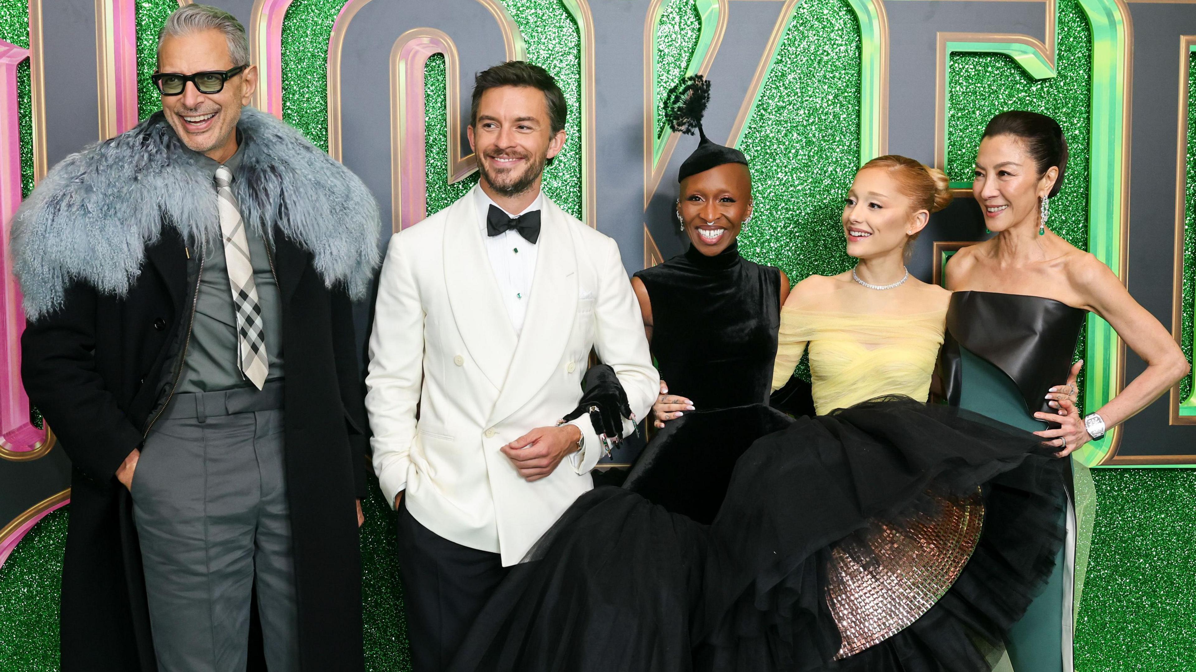 Left to right: Jeff Goldblum, Jonathan Bailey, Cynthia Erivo, Ariana Grande and Michelle Yeoh in front of a sparkly green background