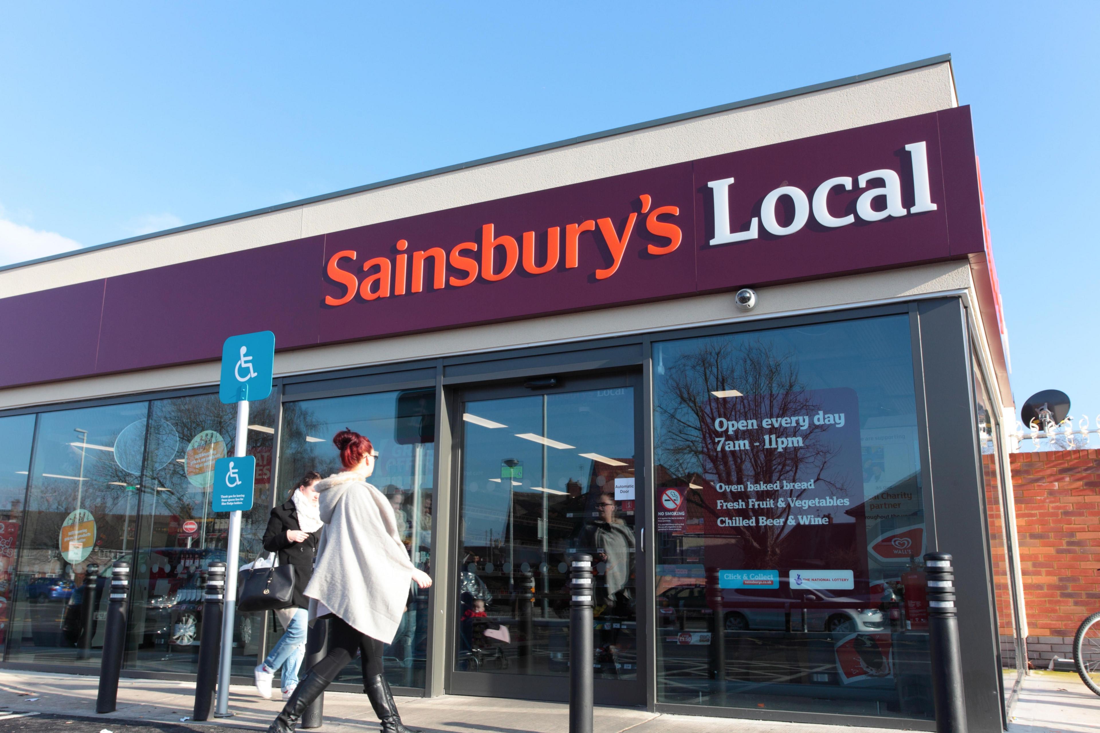 A woman walking into a Sainsbury's Local convenience store