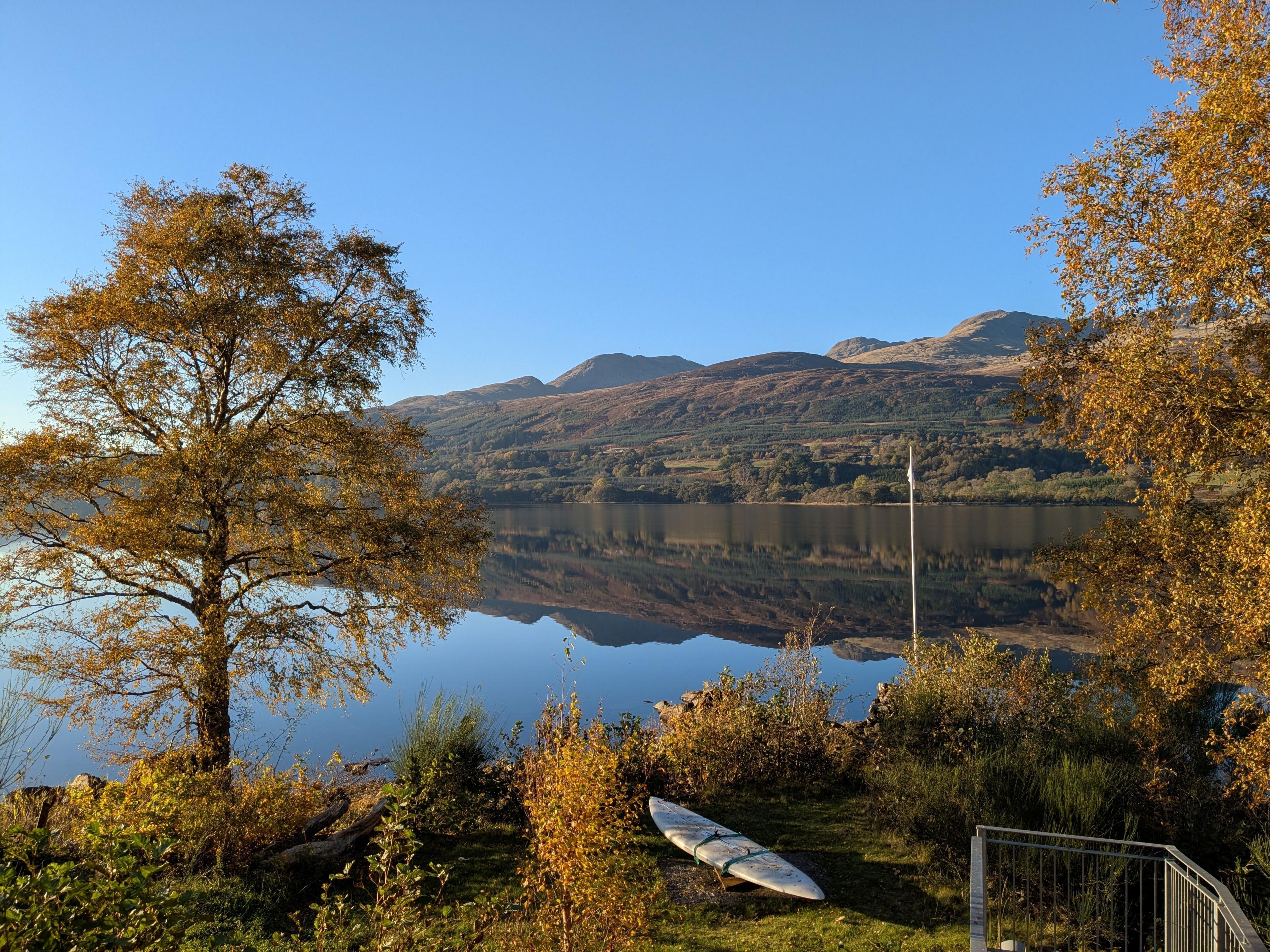 A loch on a bright autumn day. The trees are covered in orange shaded leaves