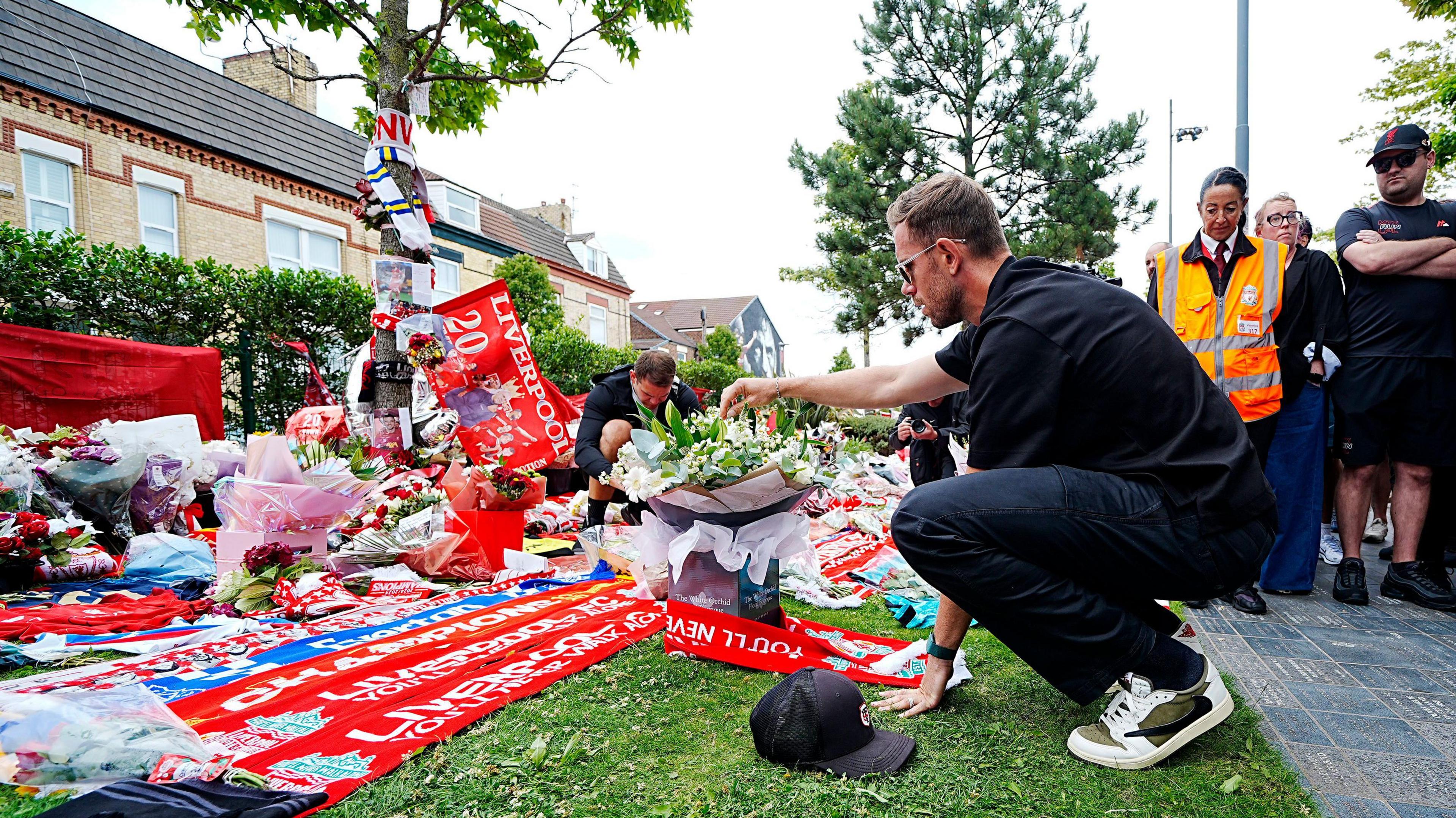Jordan Henderson crouching down and looking at the tributes left to Diogo Jota