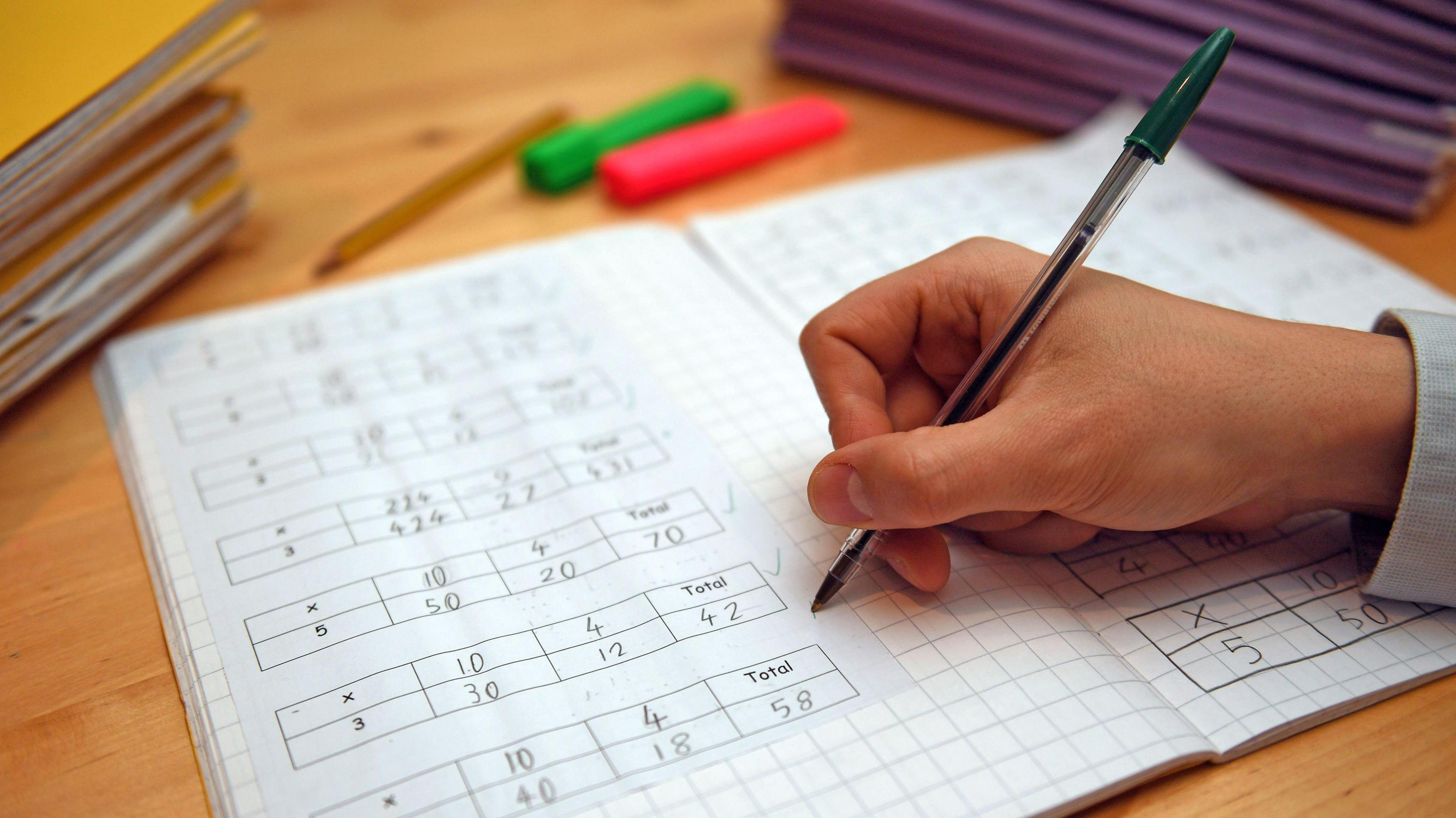 A hand holding a pen marking a school maths book