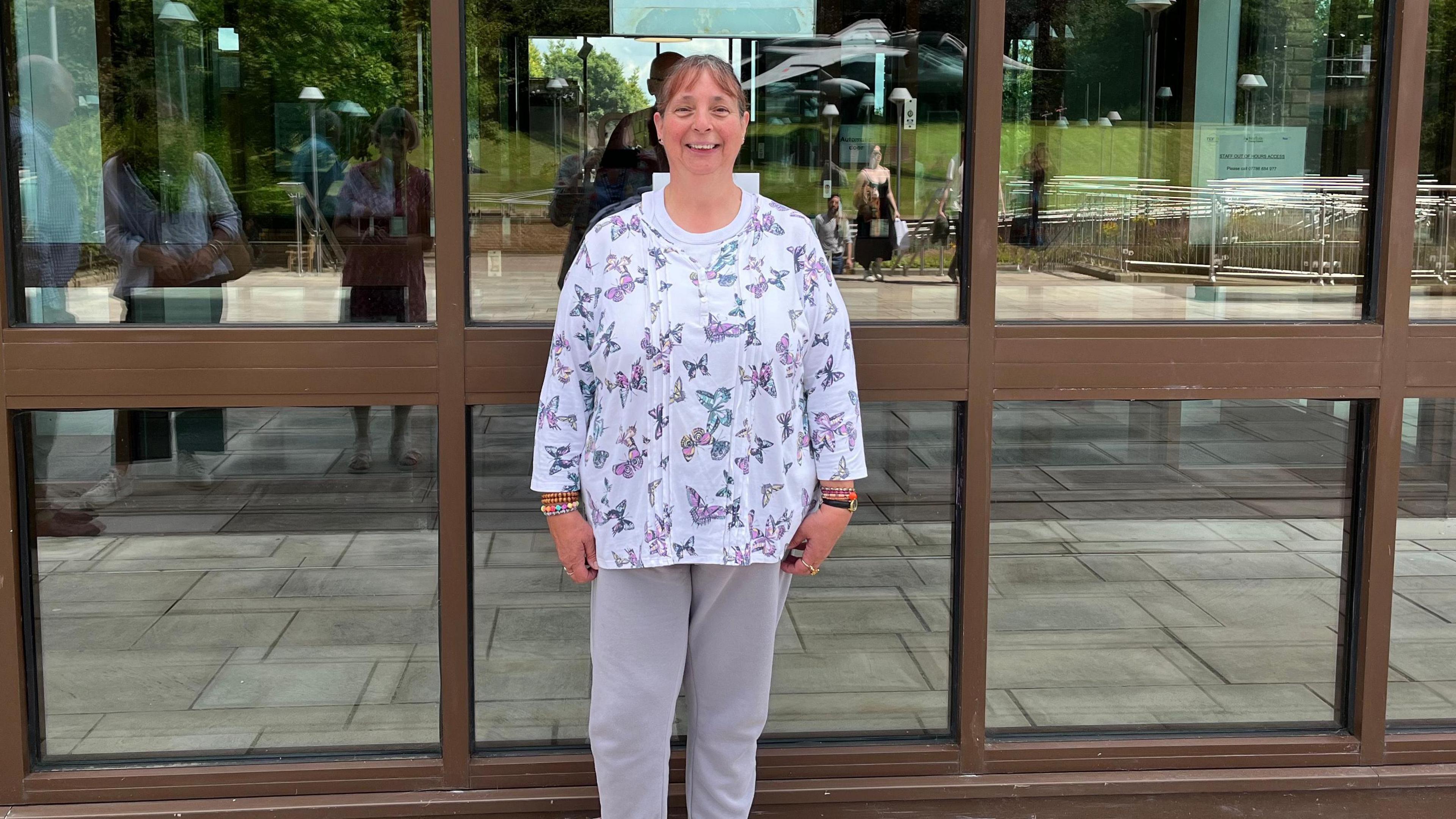 Theresa Hewitt standing in front of a door wearing a white top patterned with butterflies