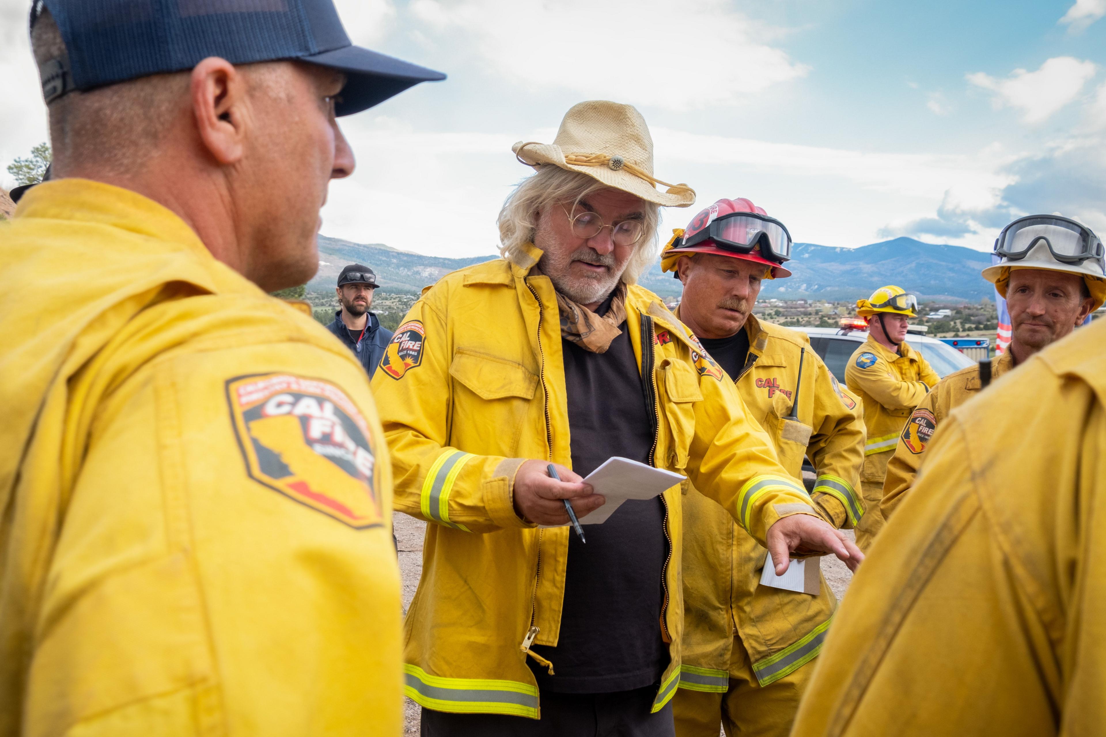 Paul Greengrass on the set of The Lost Bus in a yellow coat with firefighters and rescue workers, also in yellow uniforms