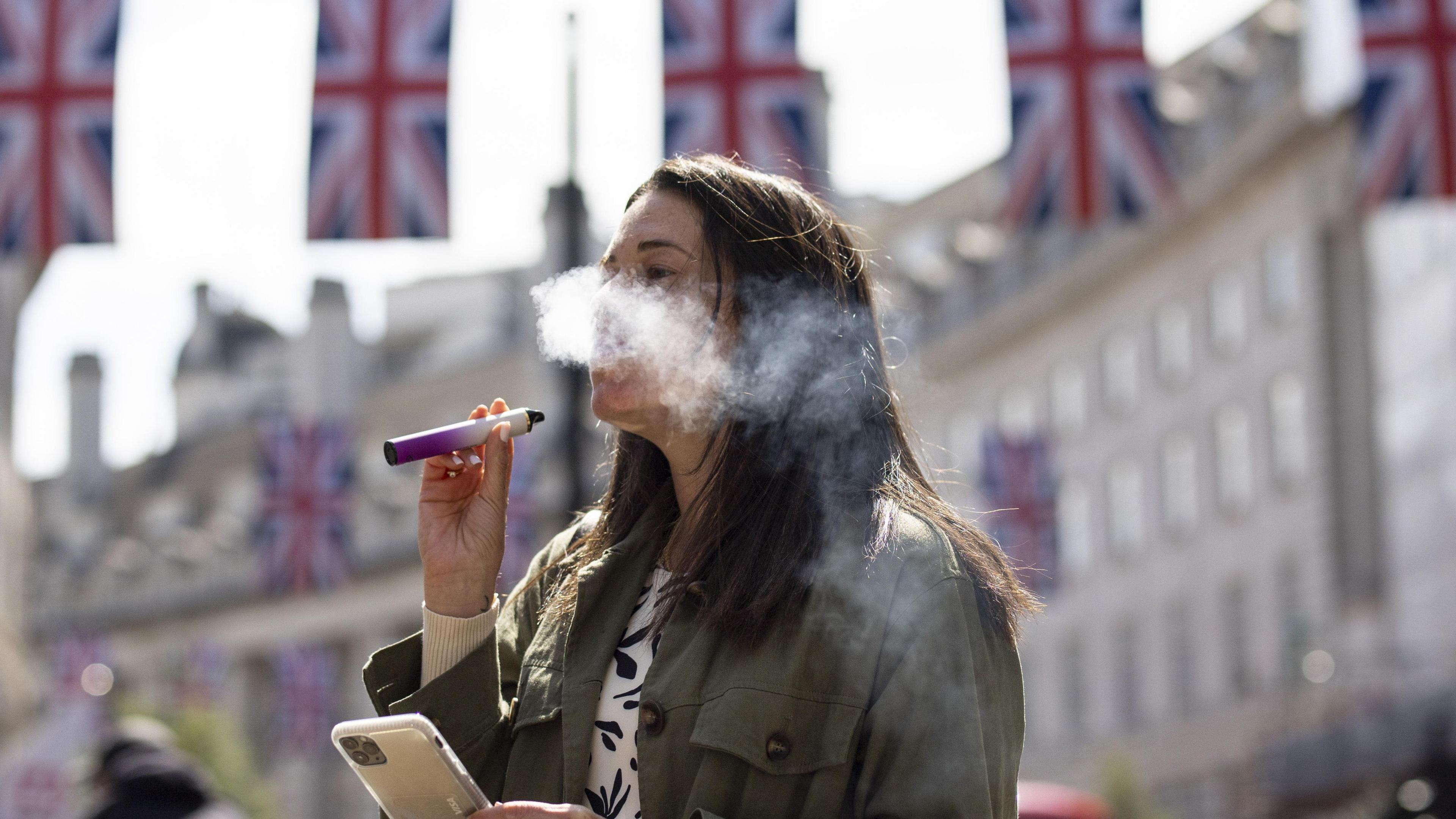 Woman smokes an e-cigarette in central London, with union jack flags in the background