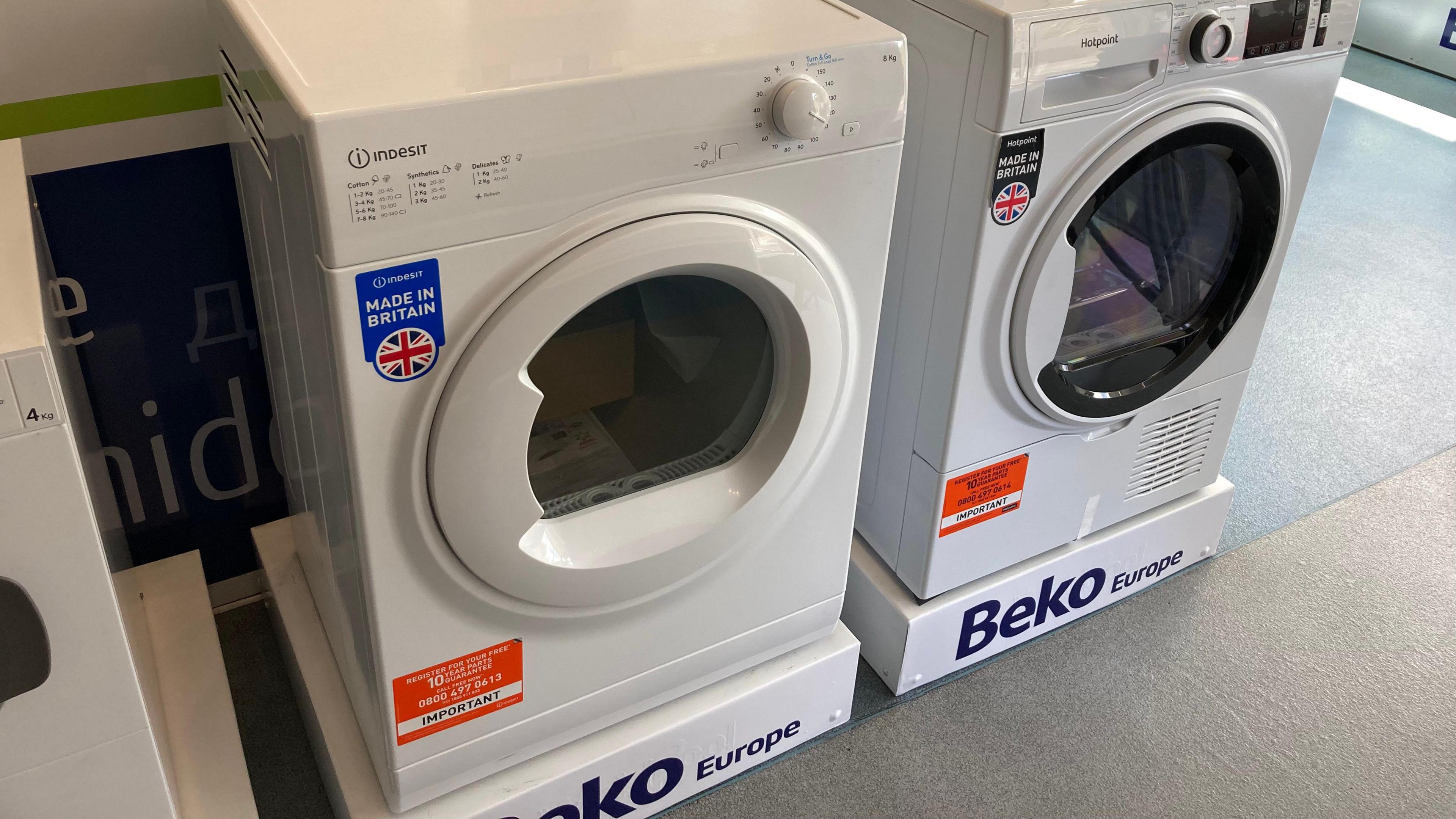 Two white tumble dryers with sitting on top of stands that say 'Beko Europe