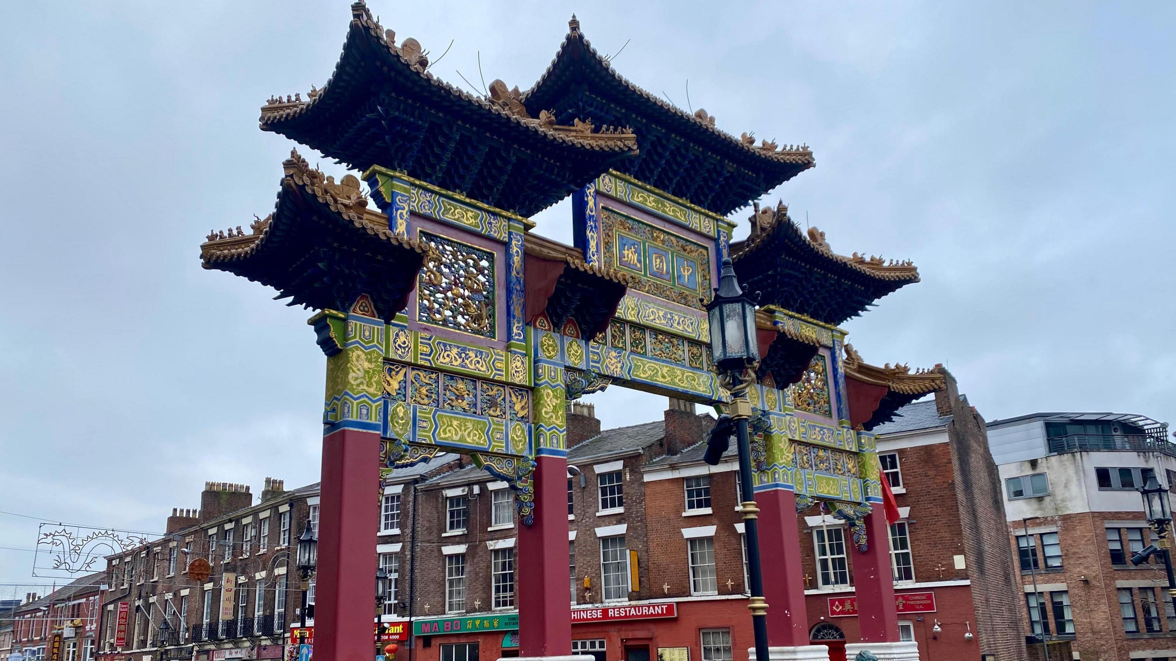 A large decorative red archway marking an entrance to Nelson Street. Behind it, there are terraced houses including Chinese restaurants on the ground floor.