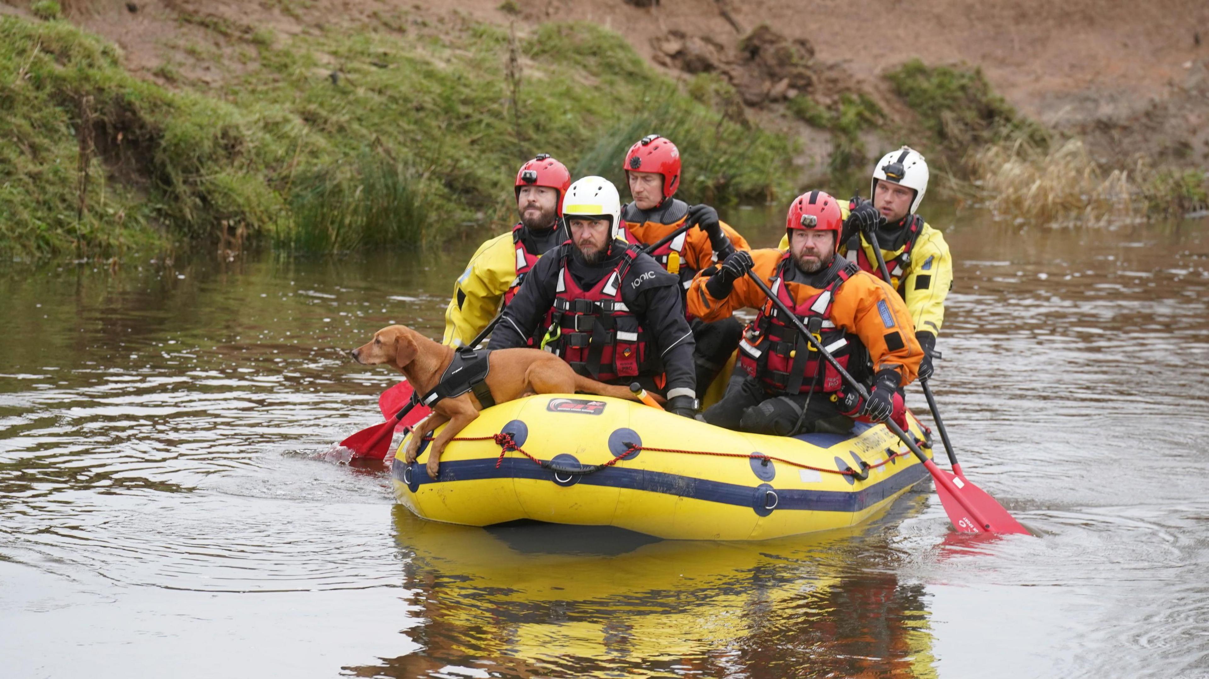 Five search and rescue team members crossing  the River Aln near Alnwick, Northumberland, on Wednesday in a yellow boat. A dog in the boat is looking out.