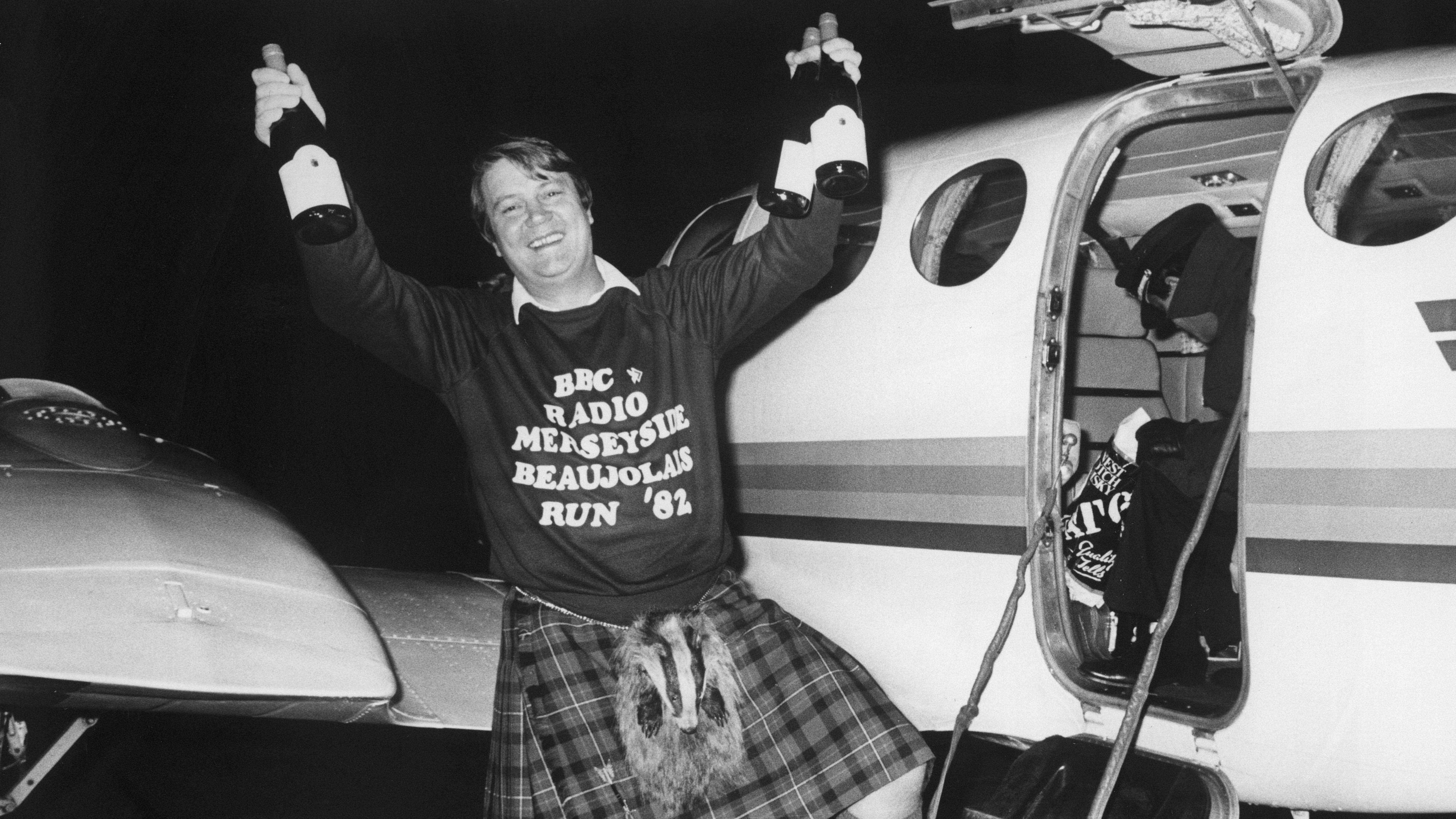 Man holding bottles of wine next to a small aircraft 