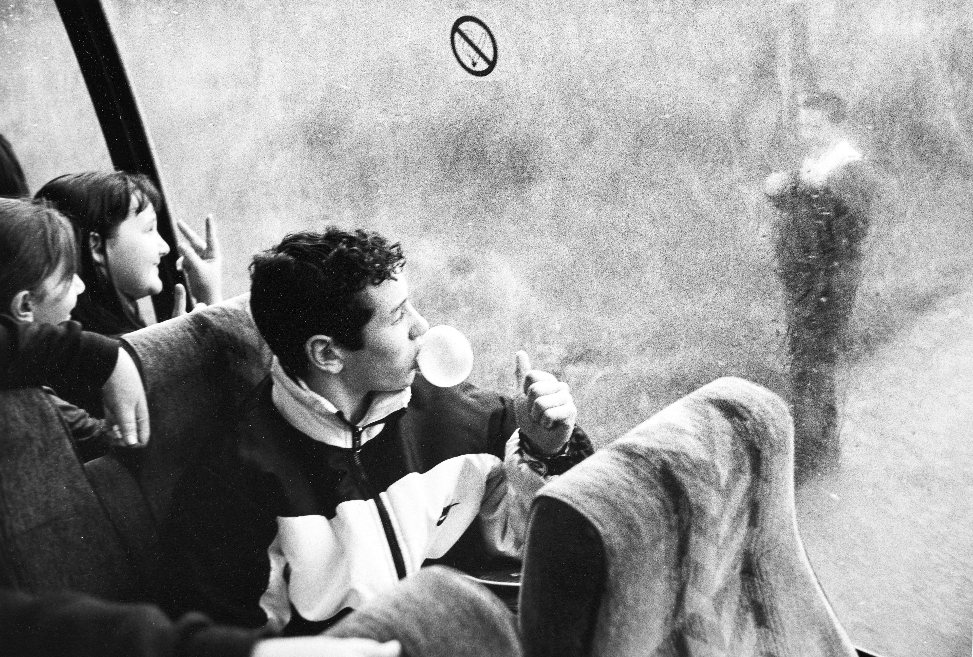 Llun du a gwyn o bobl ifanc ar fws. Mae bachgen yn chwythu bubblegum ac yn codi bawb ar blentyn sy tu allan i'r bws. Yn y sedd tu ol iddo, mae merch yn codi dau fys ar yr un plentyn. 