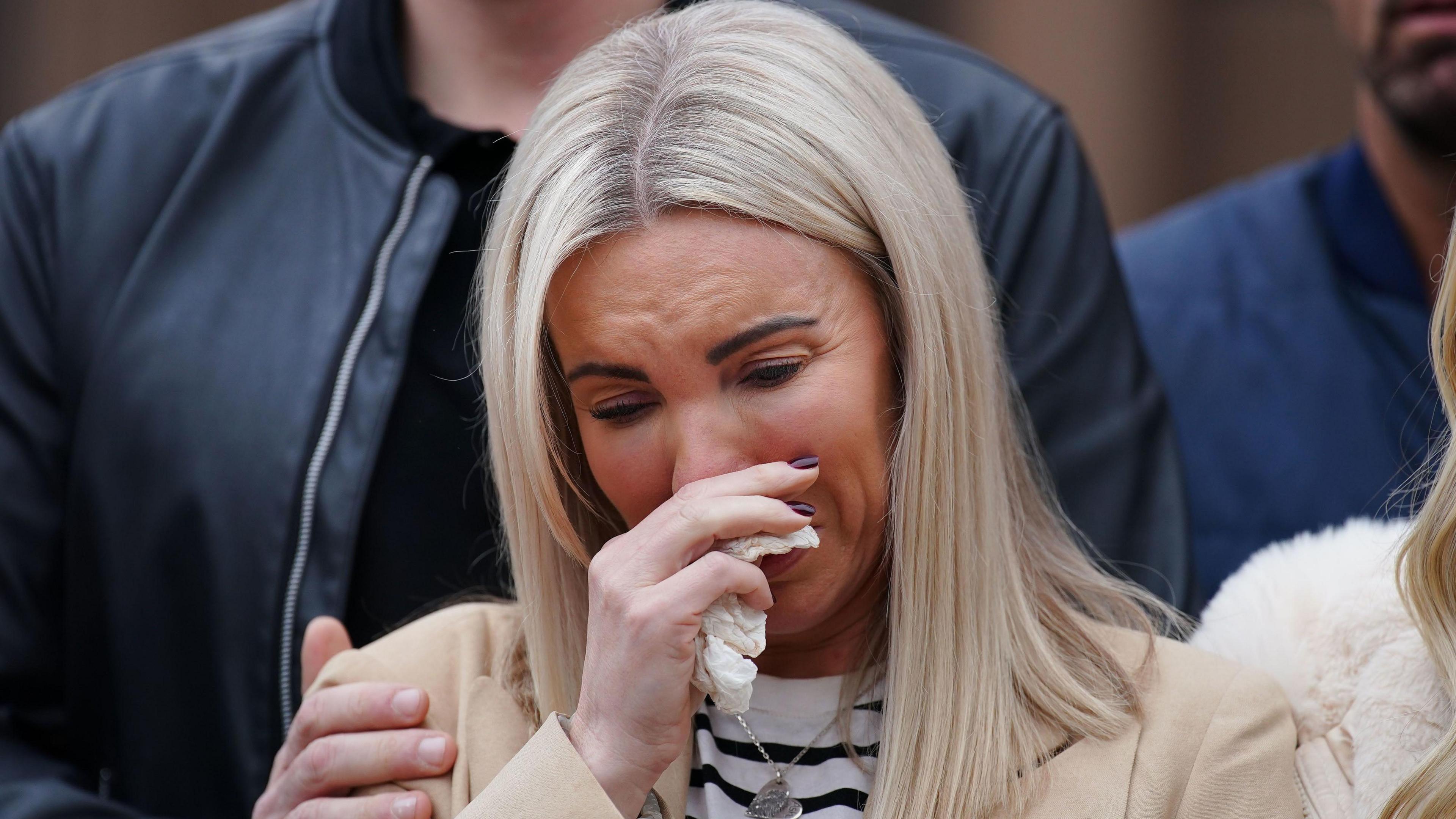 Julie Dale holds a tissue and sobs as she is comforted by family 