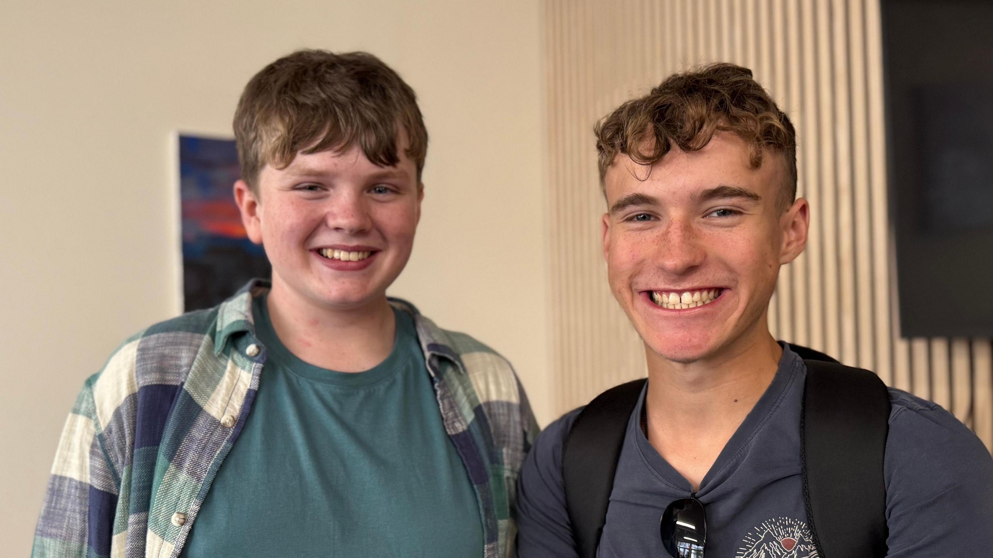 Two teenage boys in T-Shirts. One has a shirt. They both have brown hair and are smiling