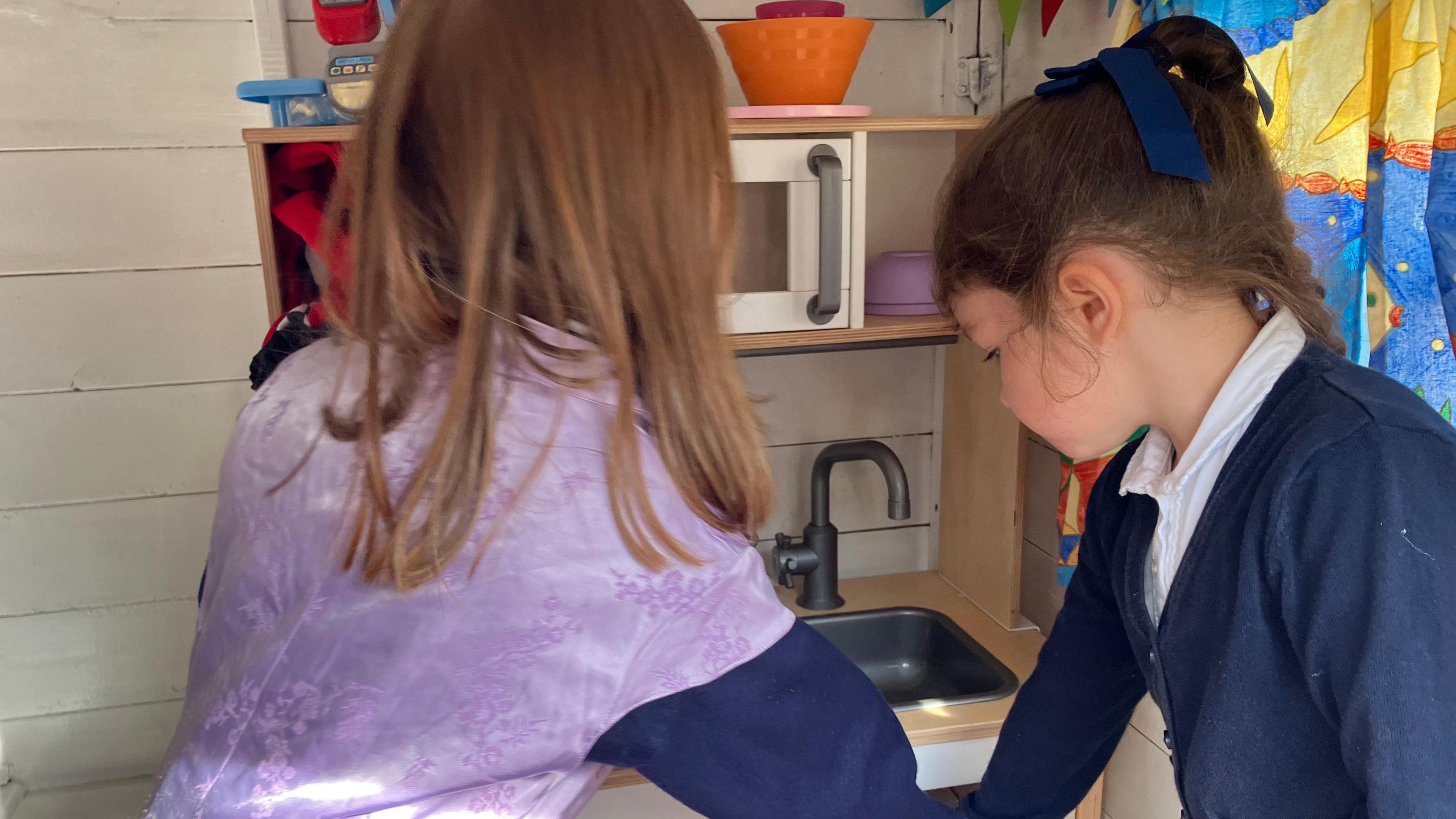 Two small girls play with a toy kitchen in the Wendy house.