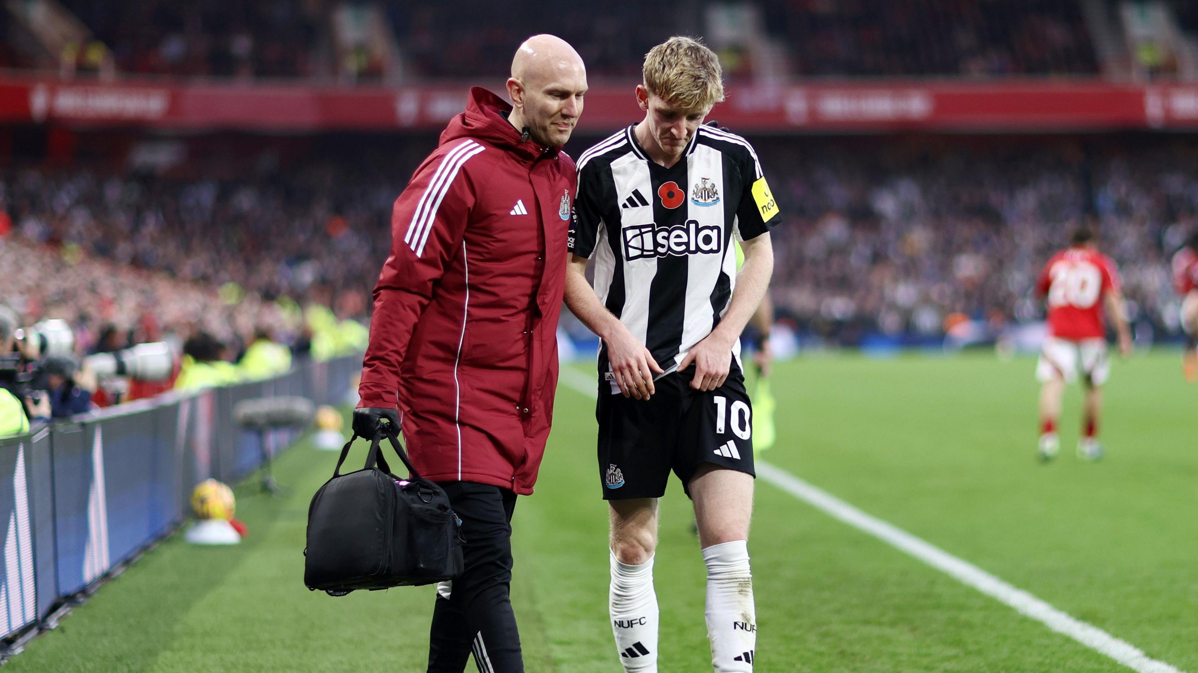 Anthony Gordon comes off the pitch at the City Ground with a Newcastle physio. 