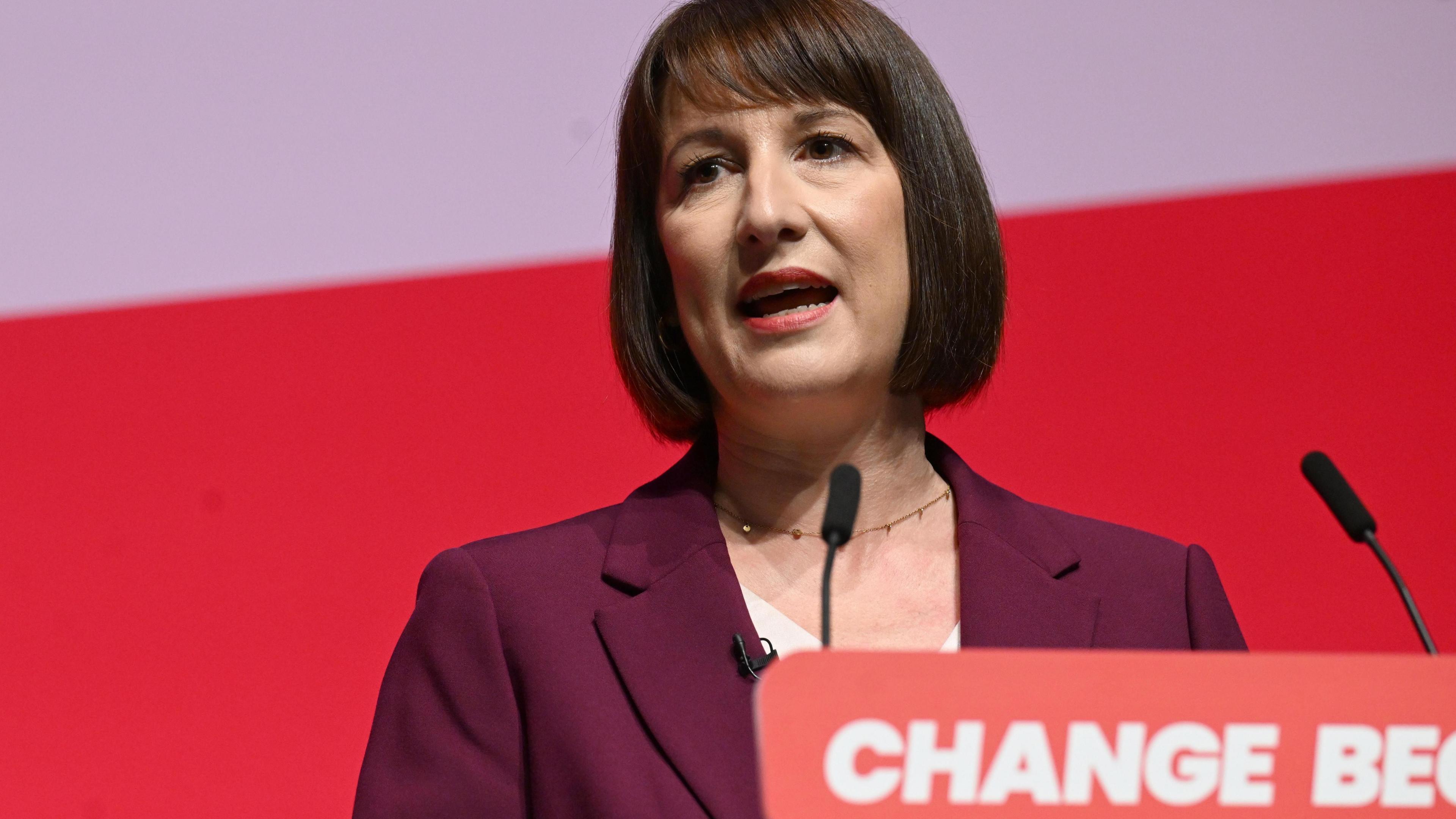 Rachel Reeves, who has brown hair in a bob, stands in front of a lectern carrying the words 'Change Begins' 