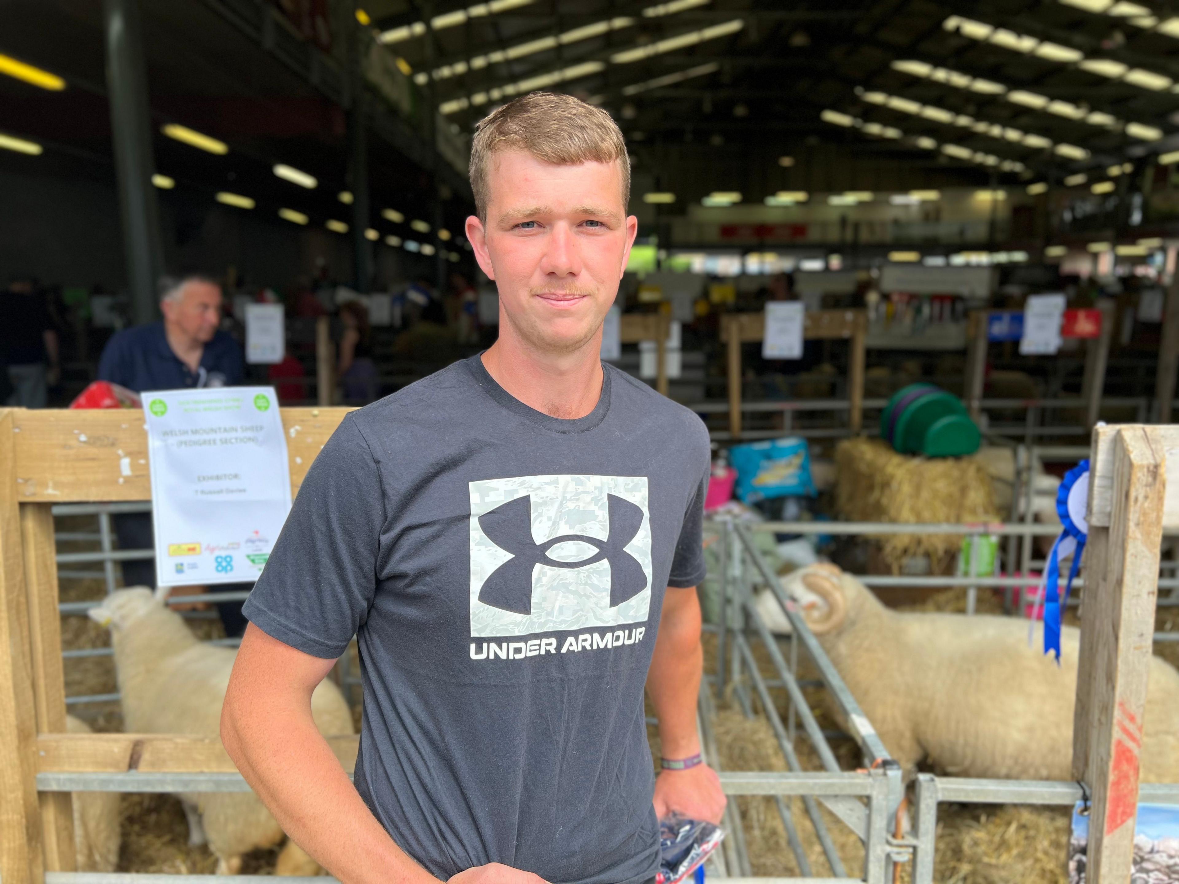 Young man in a t-shirt standing in front of a showground barn with sheep pens