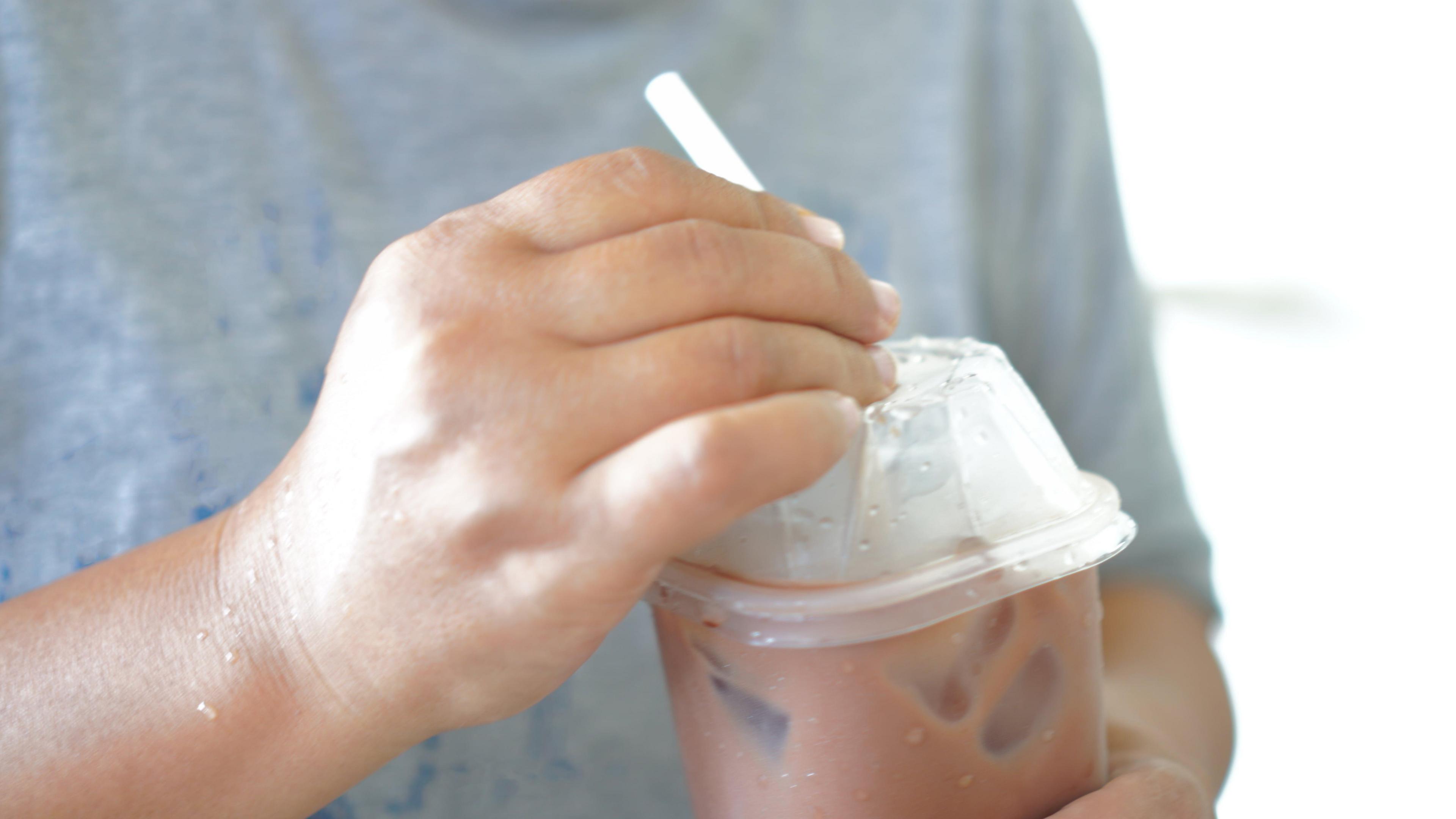 Close up of hands holding an icy drink in a plastic cup with a straw.