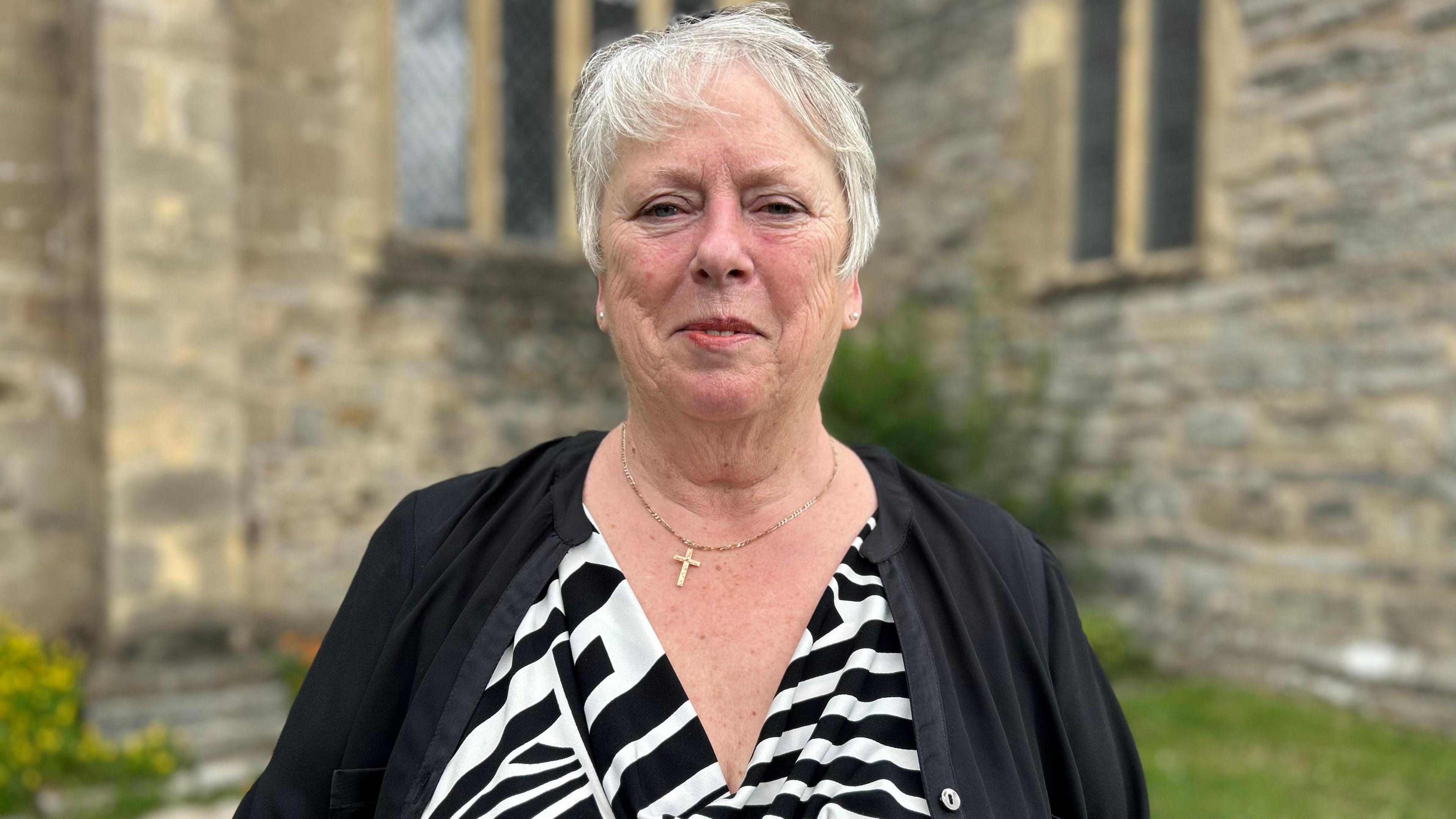 Shirley Morse wearing a black and white top stood outside the stone church