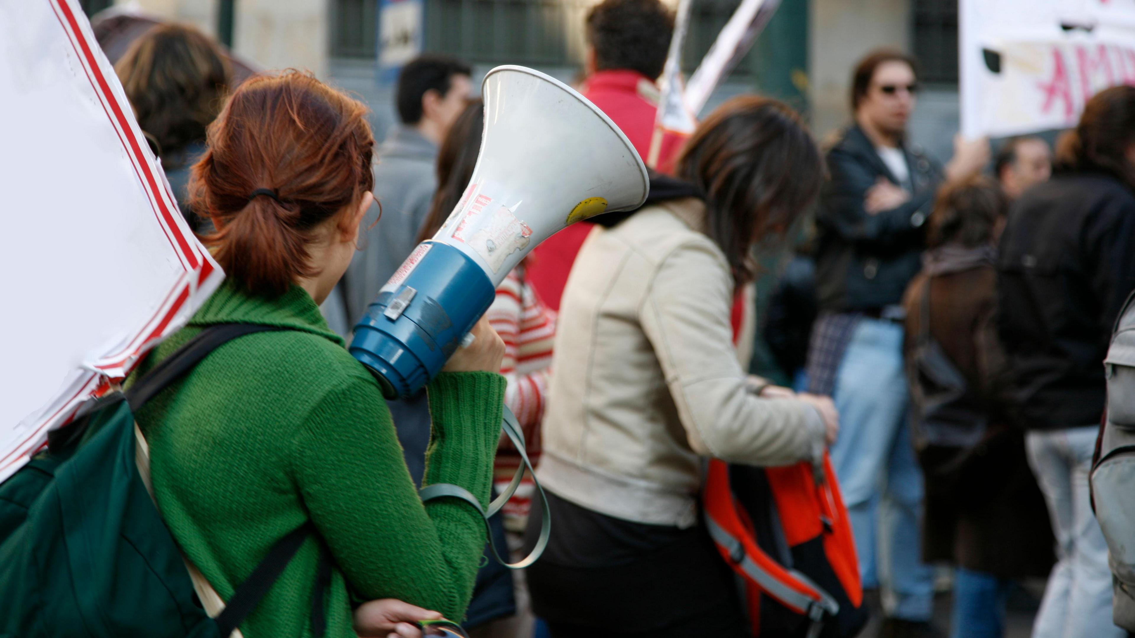 Woman facing away from camera and holding megaphone in crowd of people at protest