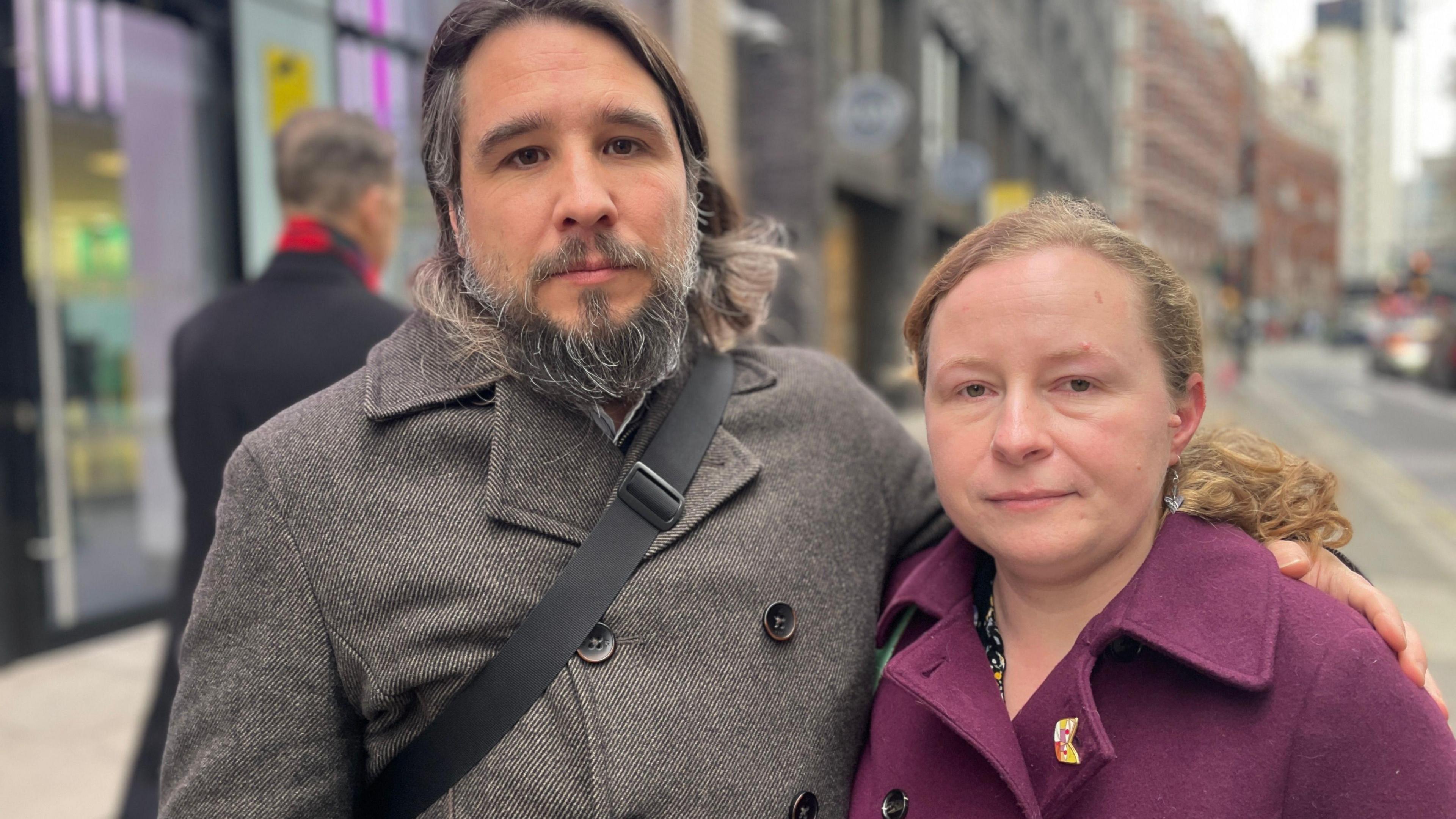 Rob Miller and Katie Fowler face the camera wearing winter coats standing outside the Department of Health offices in Westminster