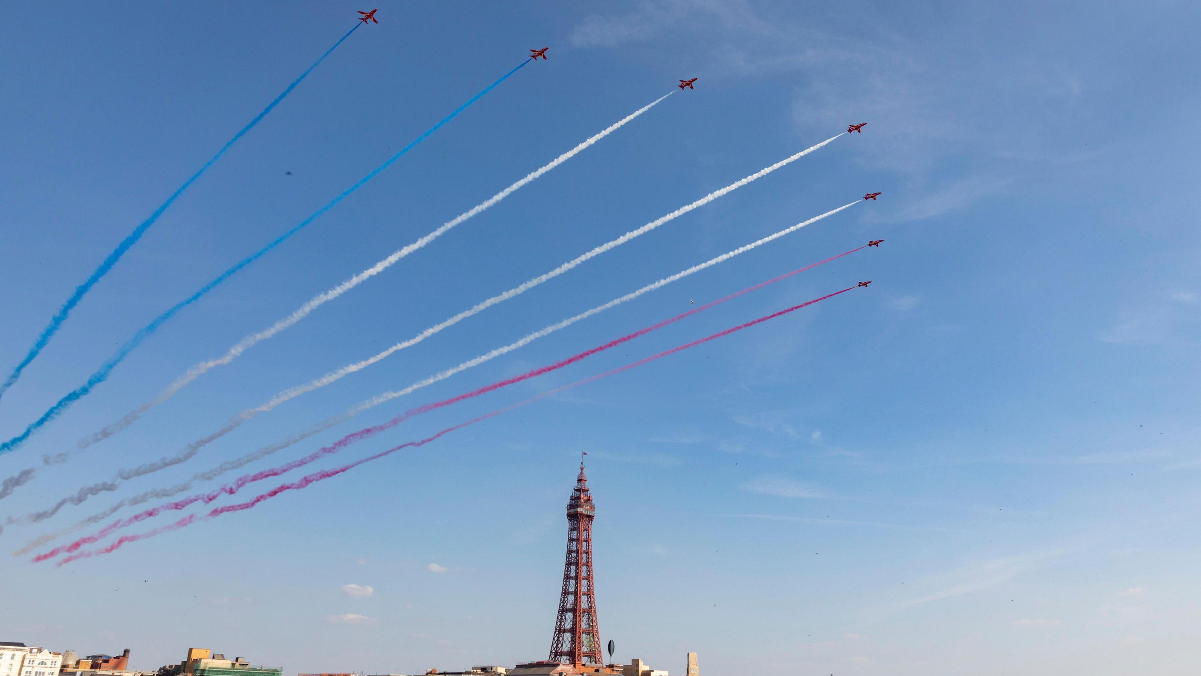 The Red Arrows fly over Blackpool Tower leaving red, white and blue vapour trails.