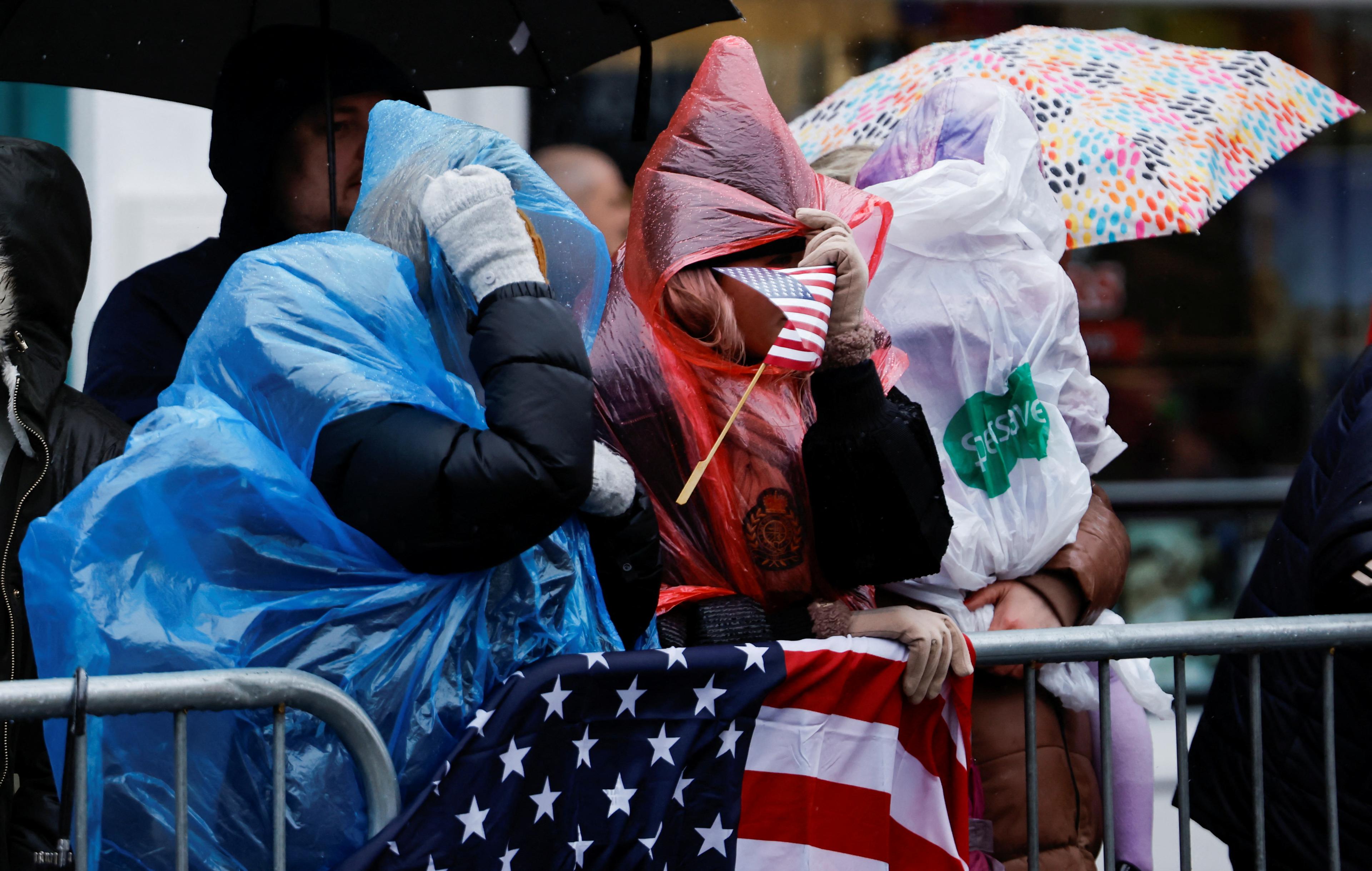 Two women wearing ponchos cower from the wind and rain as they wait to see Joe Biden