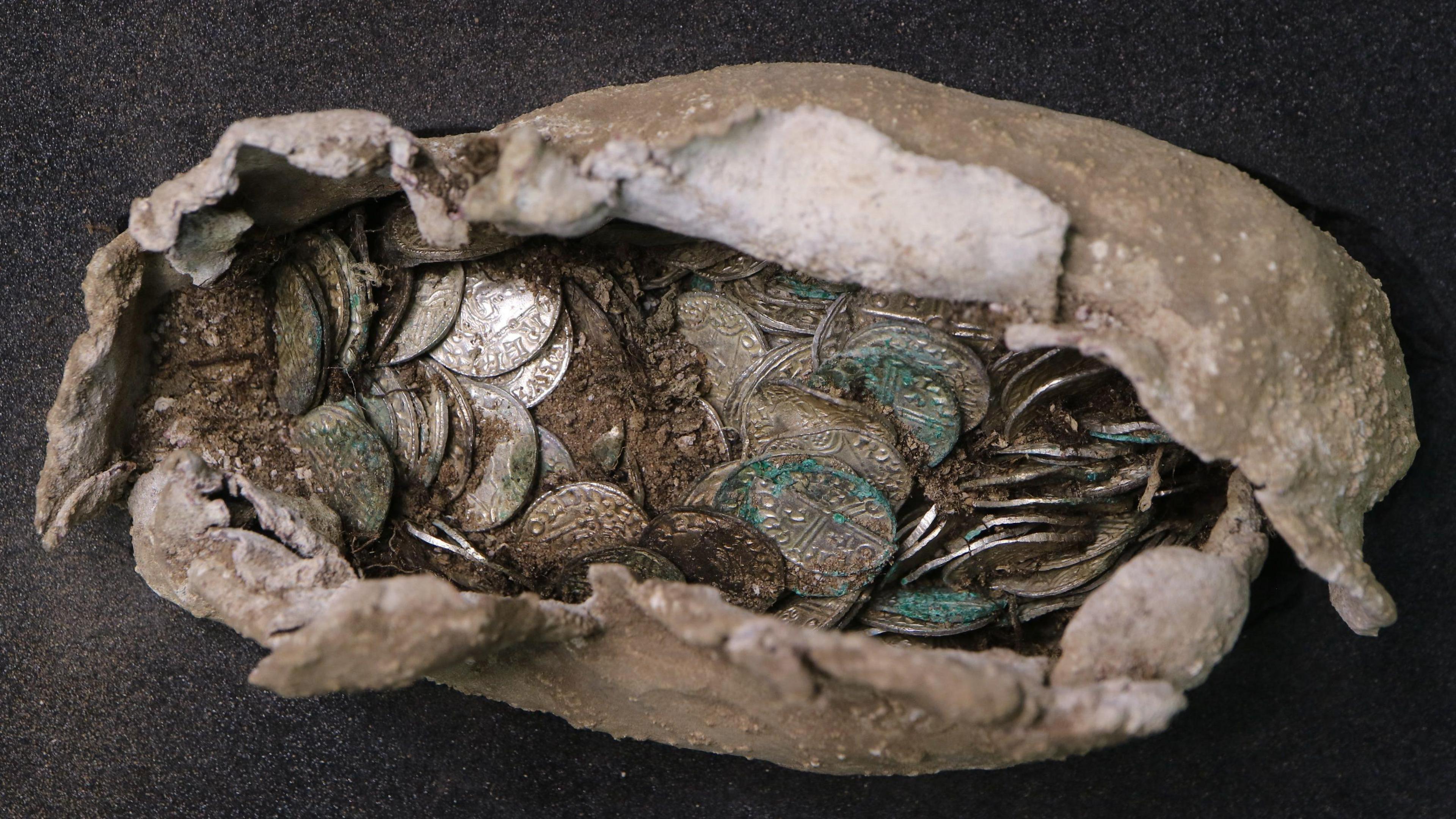 A close-up of a hoard of silver coins inside a beige pasty-shaped pouch