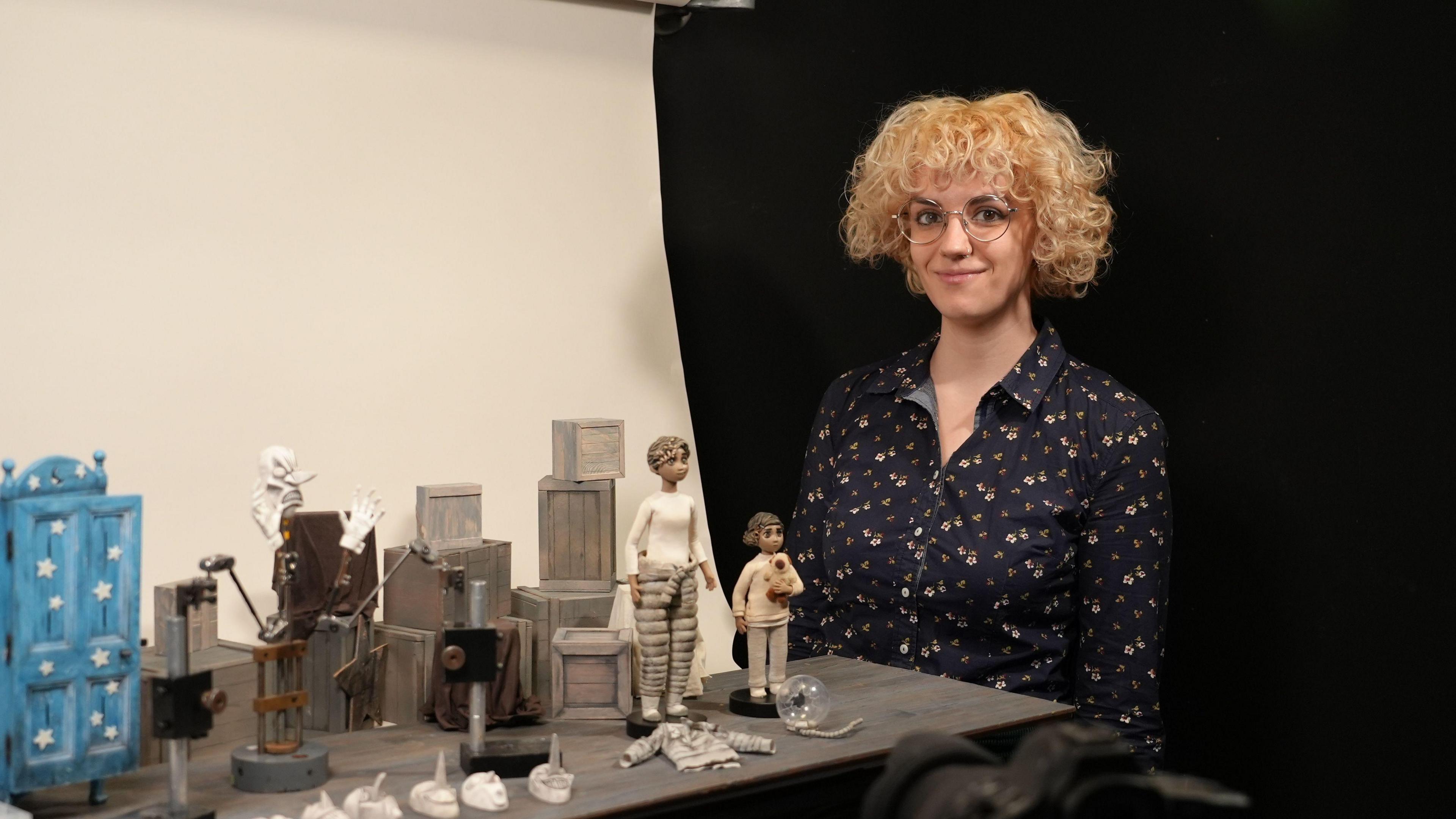 Laura Tofarides yn sefyll gyda phrif gymeriadau ei ffilm fer newydd. Mae gan Laura wallt golau a chyrliog ac mae'n gwisgo sbectol a chrys blodeuog.