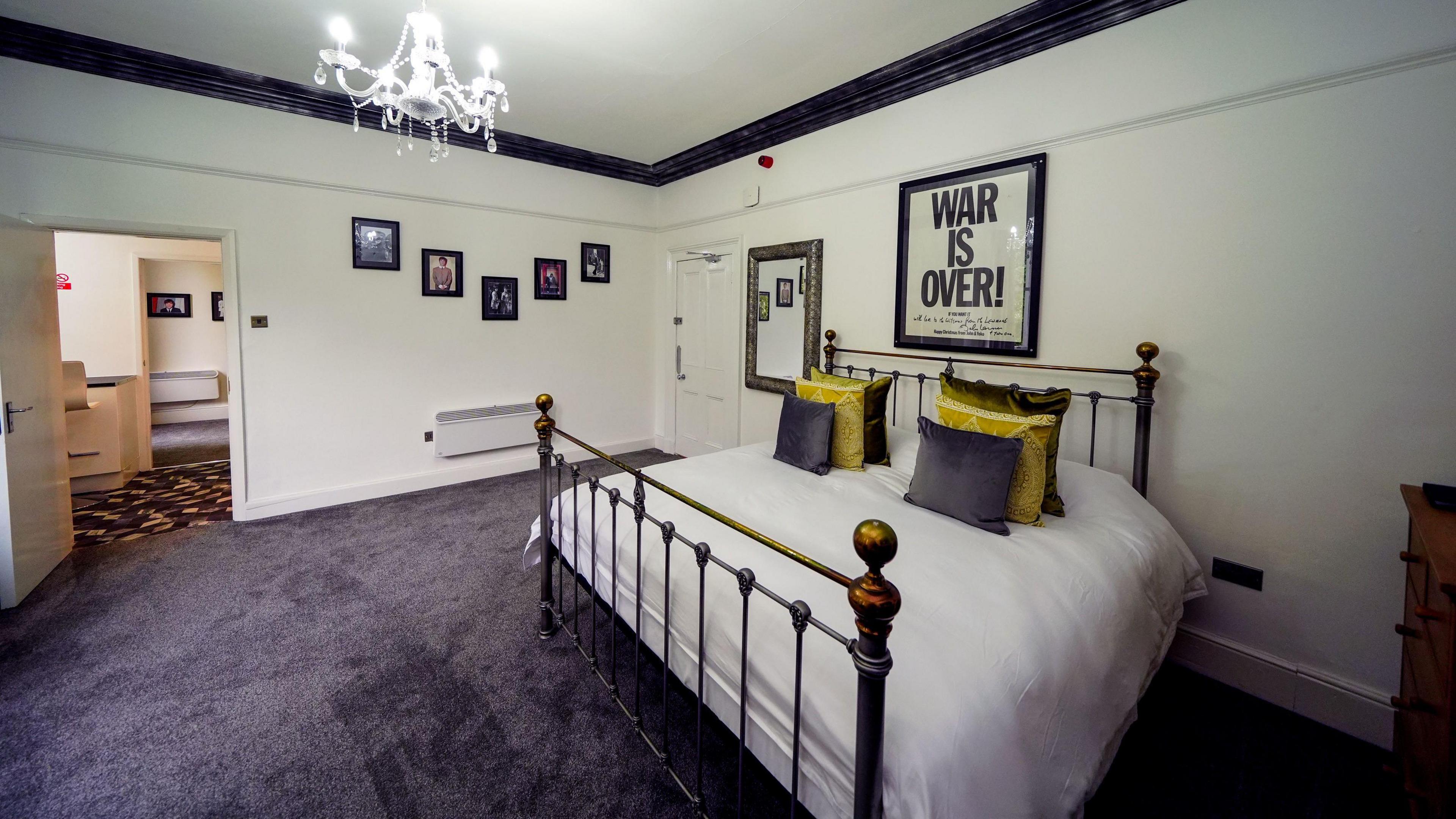 Themed room with a double bed with white sheets and a War Is Over framed poster above the bed.