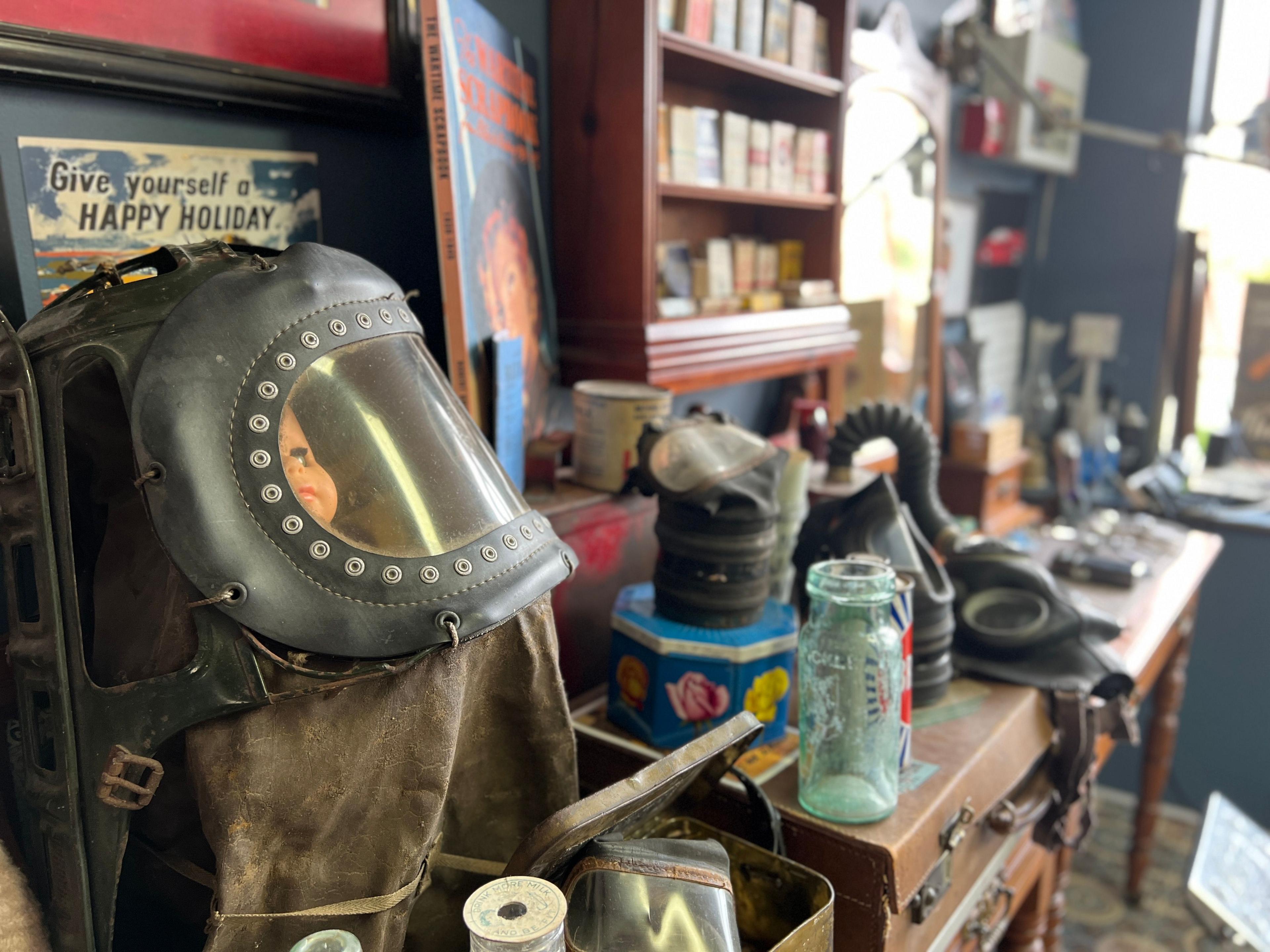 A selection of wartime gas masks rest on a table alongside cigarette packets and glass jars