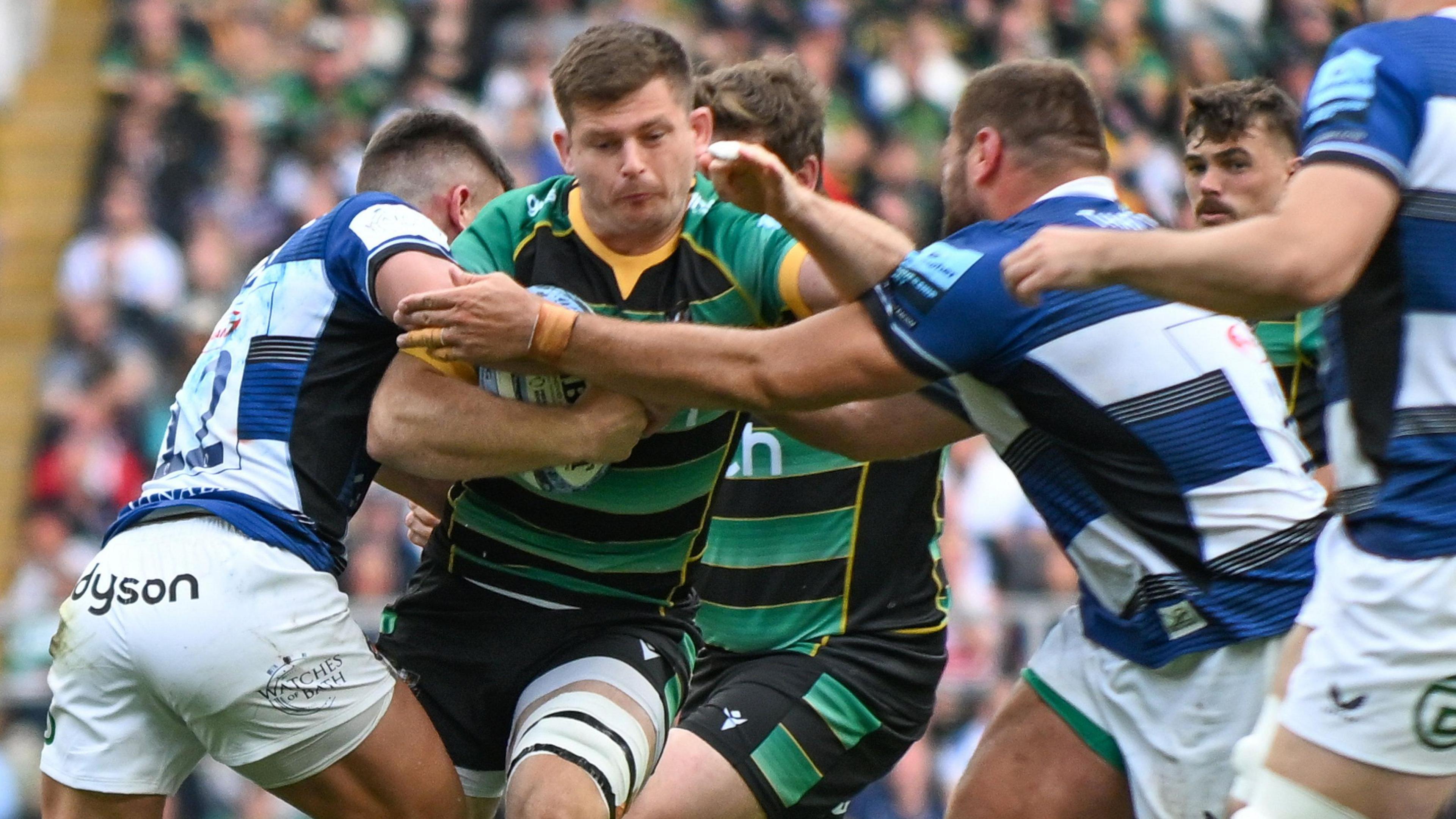 Sam Graham holding a ball and being tackled by two Bath players