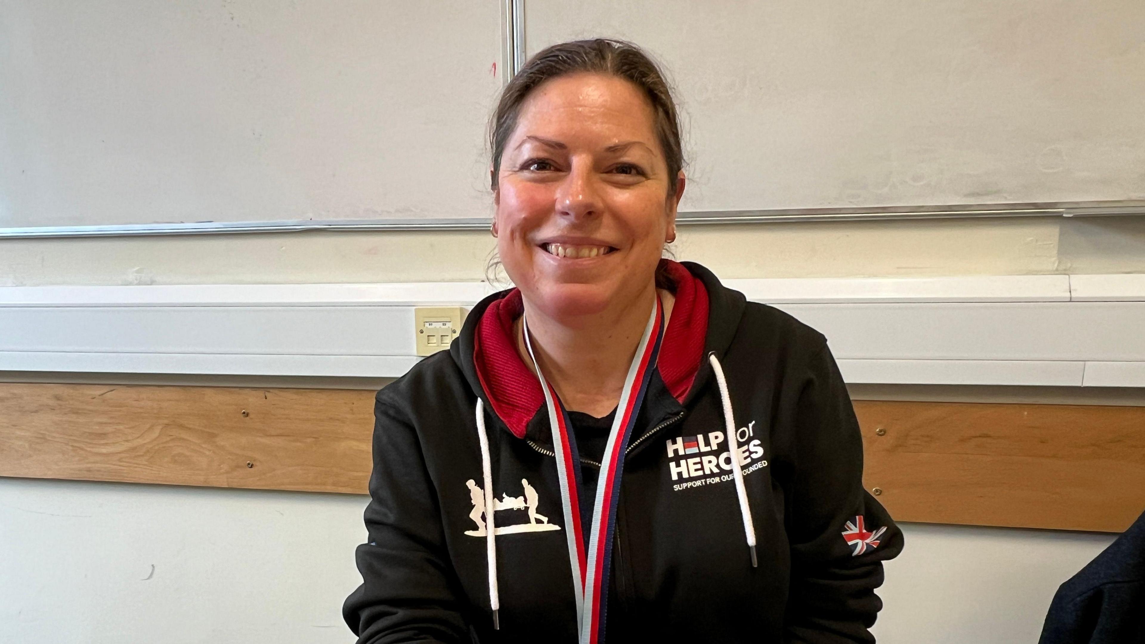 Women with dark hair smiling at the camera. She has a Help for Heroes hoodie on with a GB flag on the side.