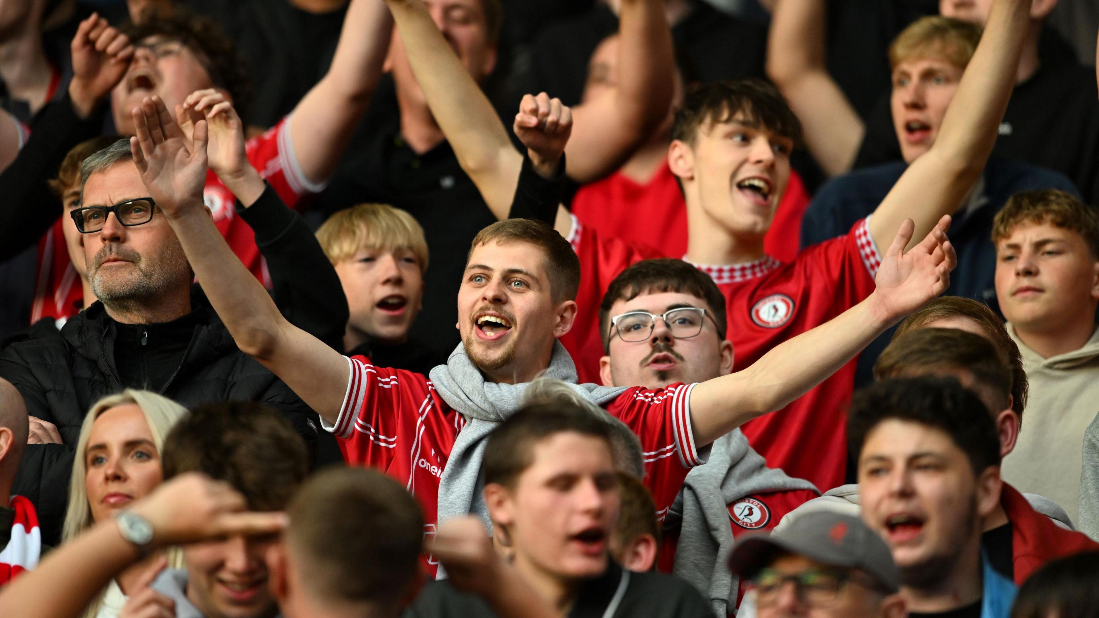Bristol City fans, many of them young men, sing in support of their team during the play-off match with Sheffield United at Ashton Gate, with their arms aloft