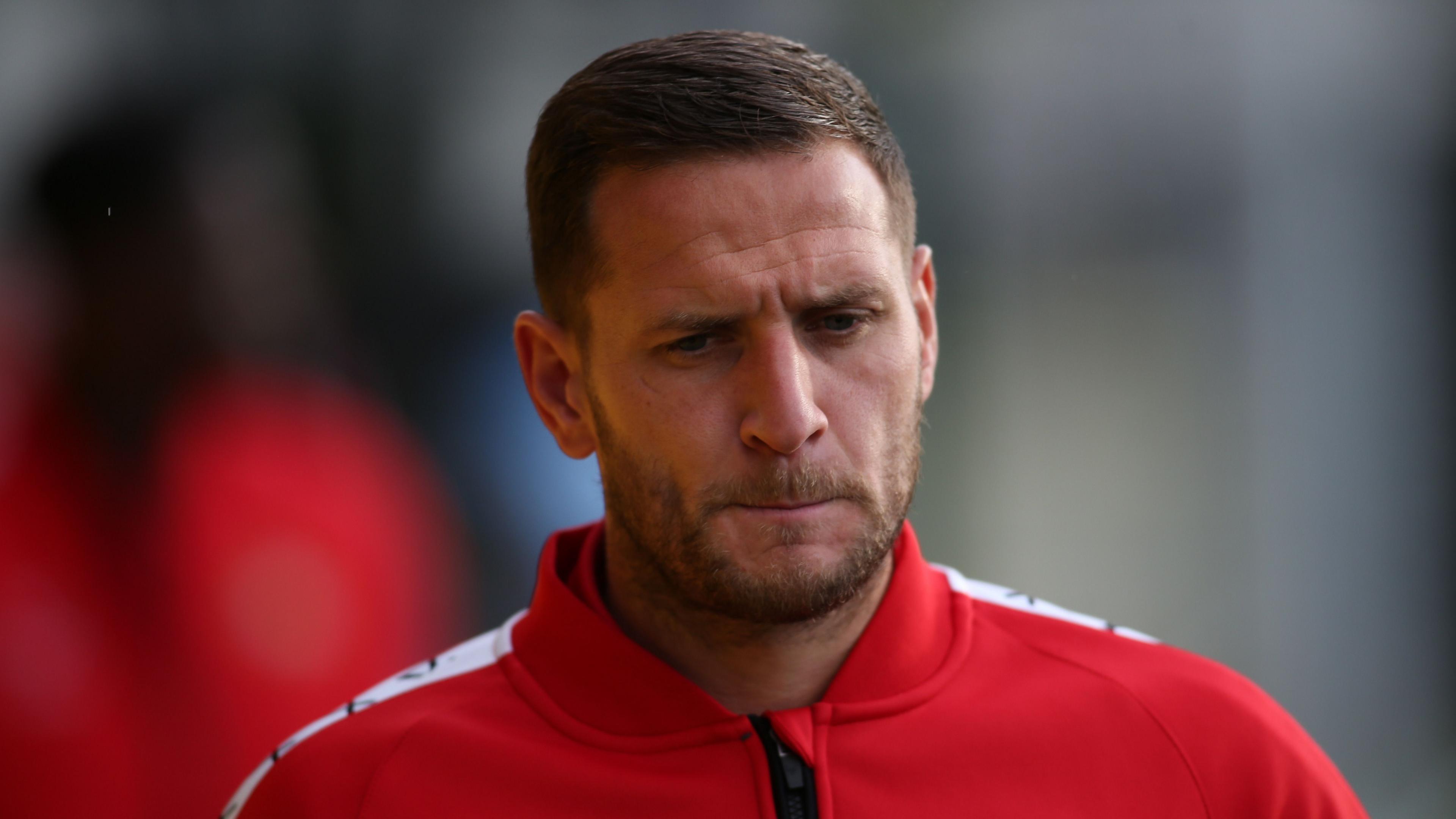 Billy Sharp is wearing a Doncaster tracksuit top and is frowning which causes creases on his forehead and in between his eyebrows.