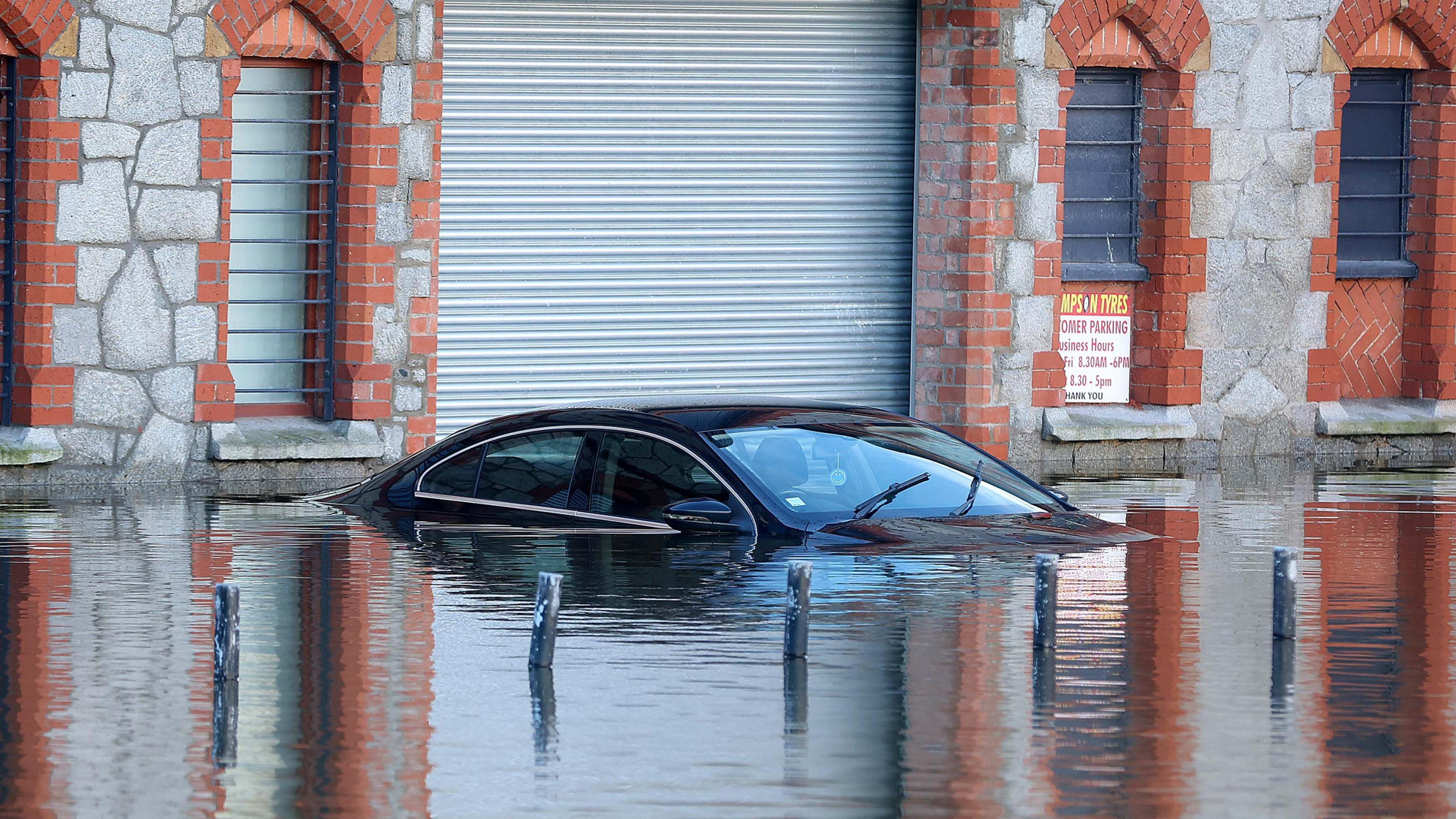 A car part submerged underwater with a brick building with a metal shutter in the background.