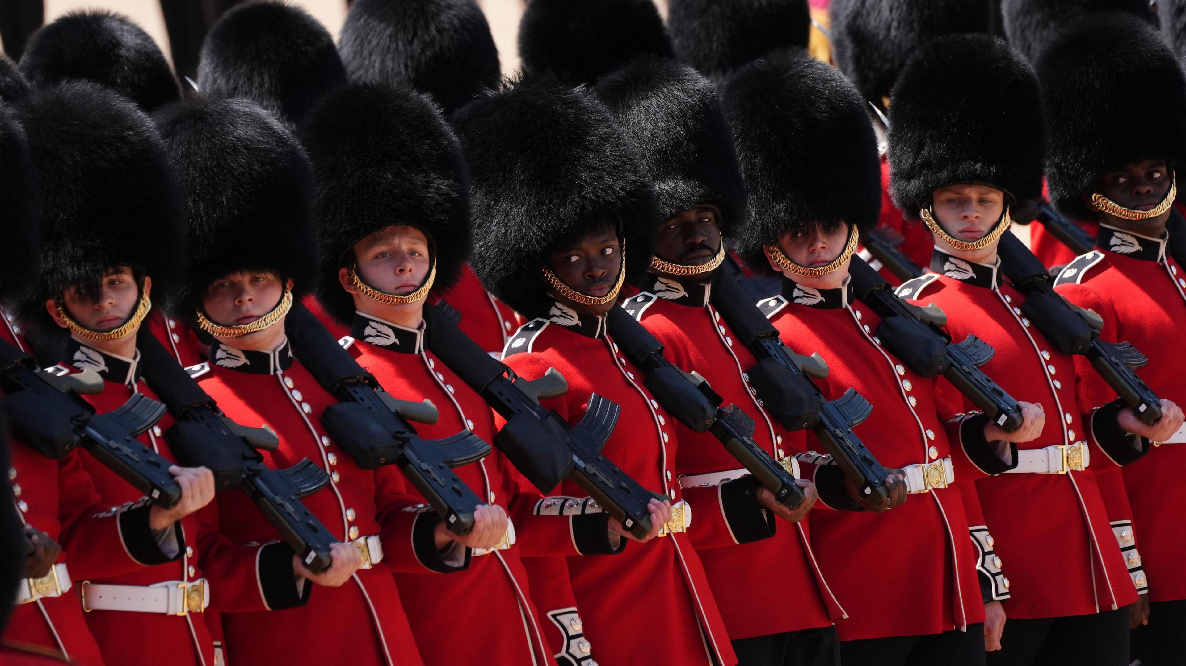 Scots Guards line up in uniform holding rifles in one hand, resting on their shoulder
