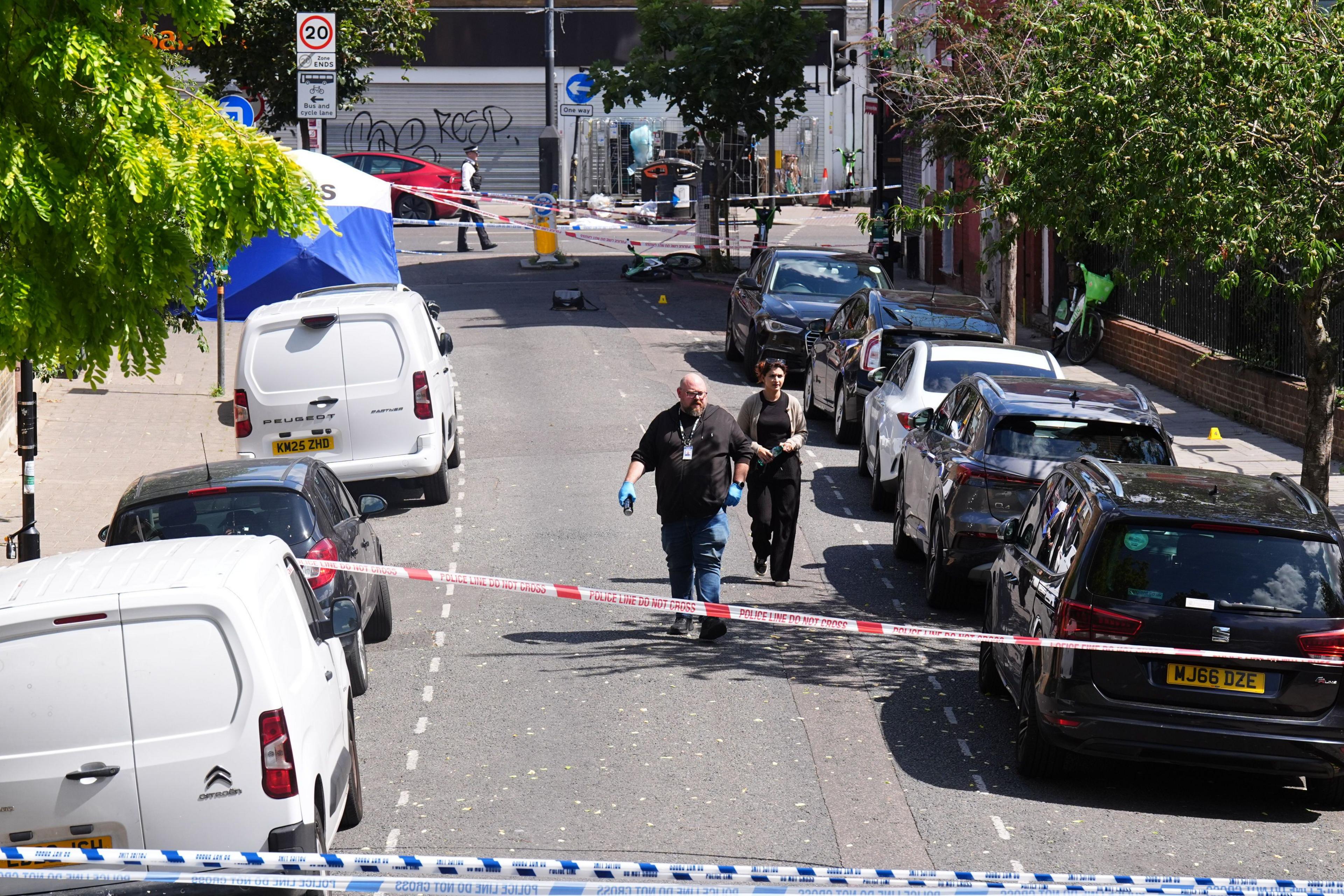A man wearing blue surgical gloves and woman walk down the middle of the road between police cordons