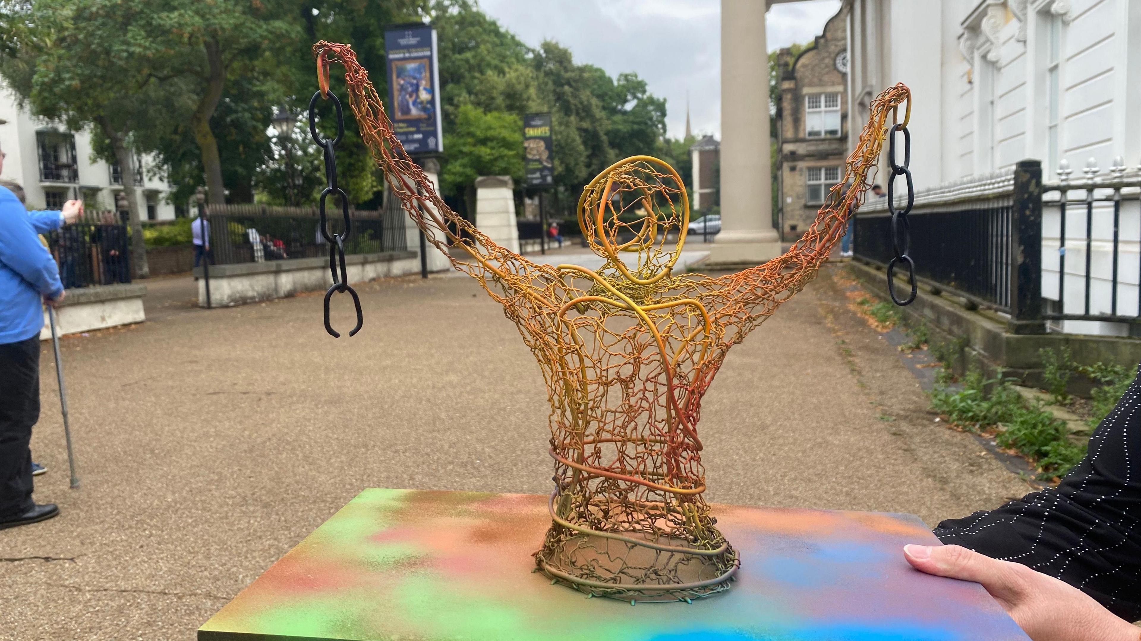 An orange, yellow and gold statue on a multi-coloured plinth