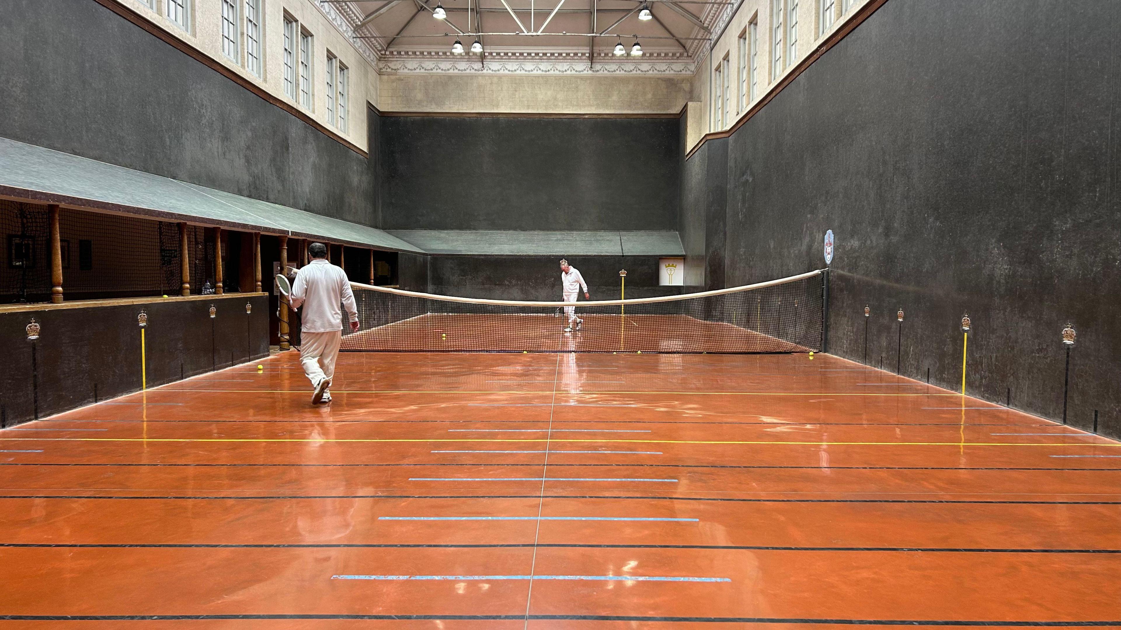 A real tennis court. the floor is large and split halfway by a net. It is surrounded by black walls - some of which are sloped.