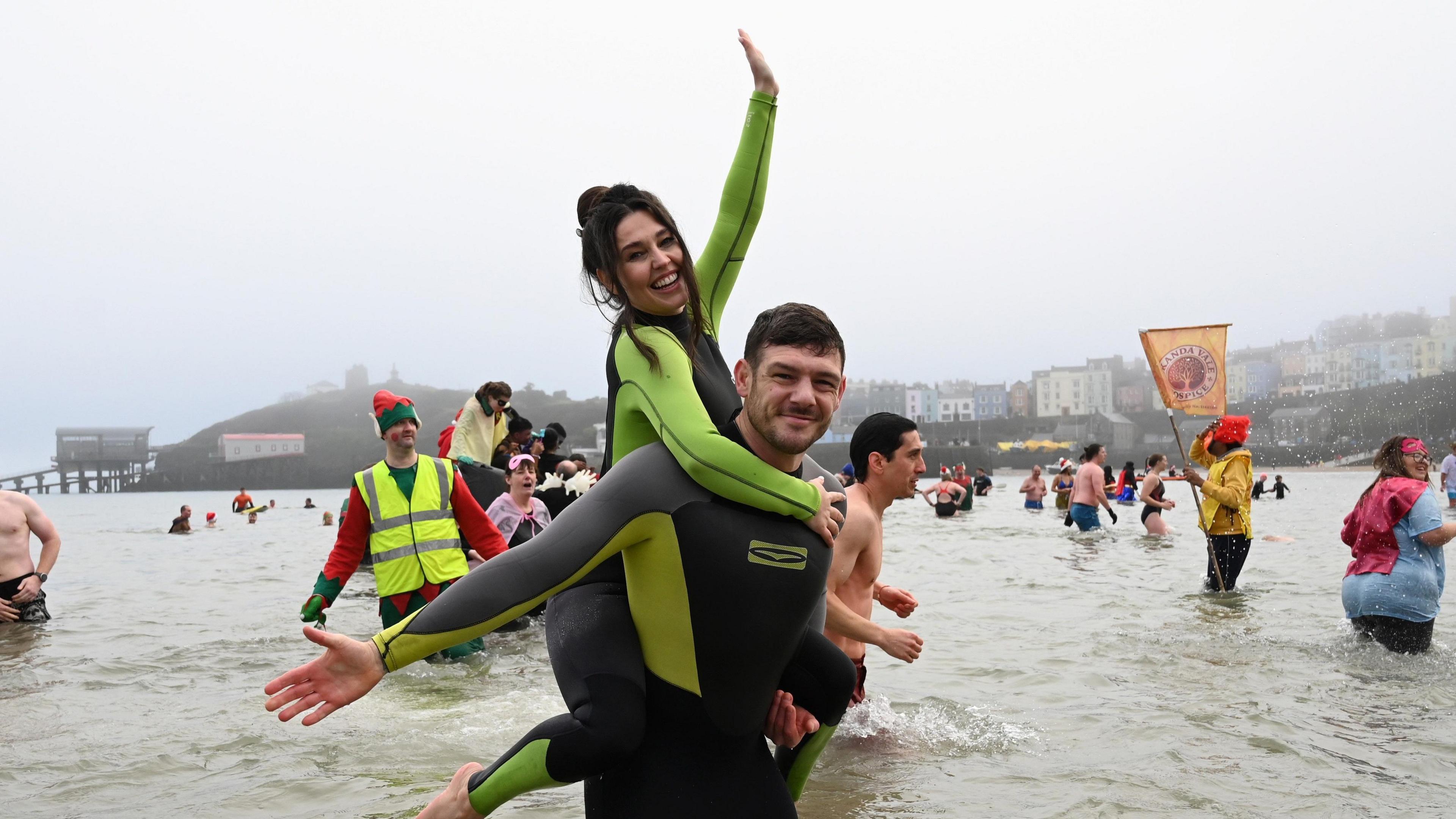 Philip Frith holding Victoria Tansey on his back after a successful proposal. Swimmers are visible behind them 