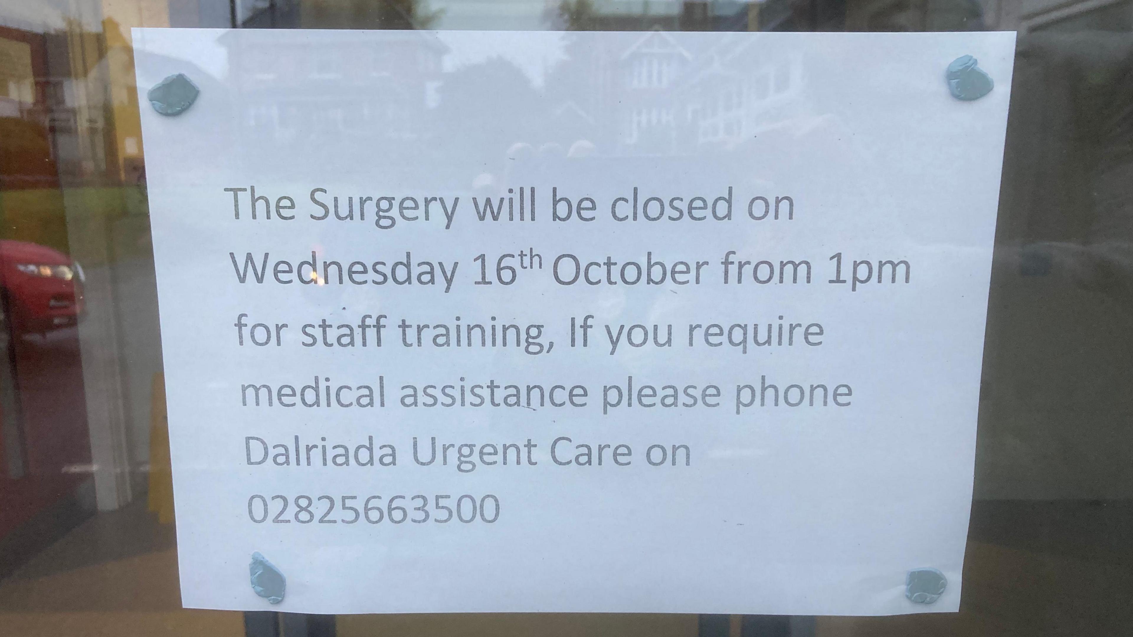 A sign is blue-tacked to a window. It says: "The Surgery will be closed on Wednesday 16th October from 1pm for staff training. If you require medical assistance please phone Dalriada Urgent Care on 02825663500."