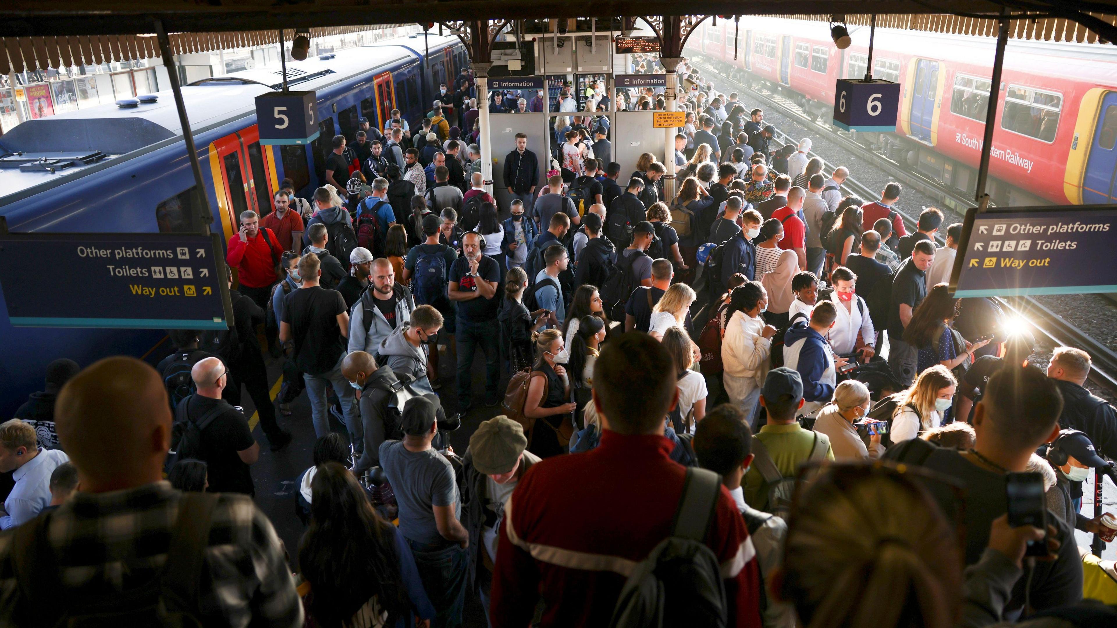 An image of Clapham Junction station during rush hour. The platform is overcrowded with people and a train is on the left platform