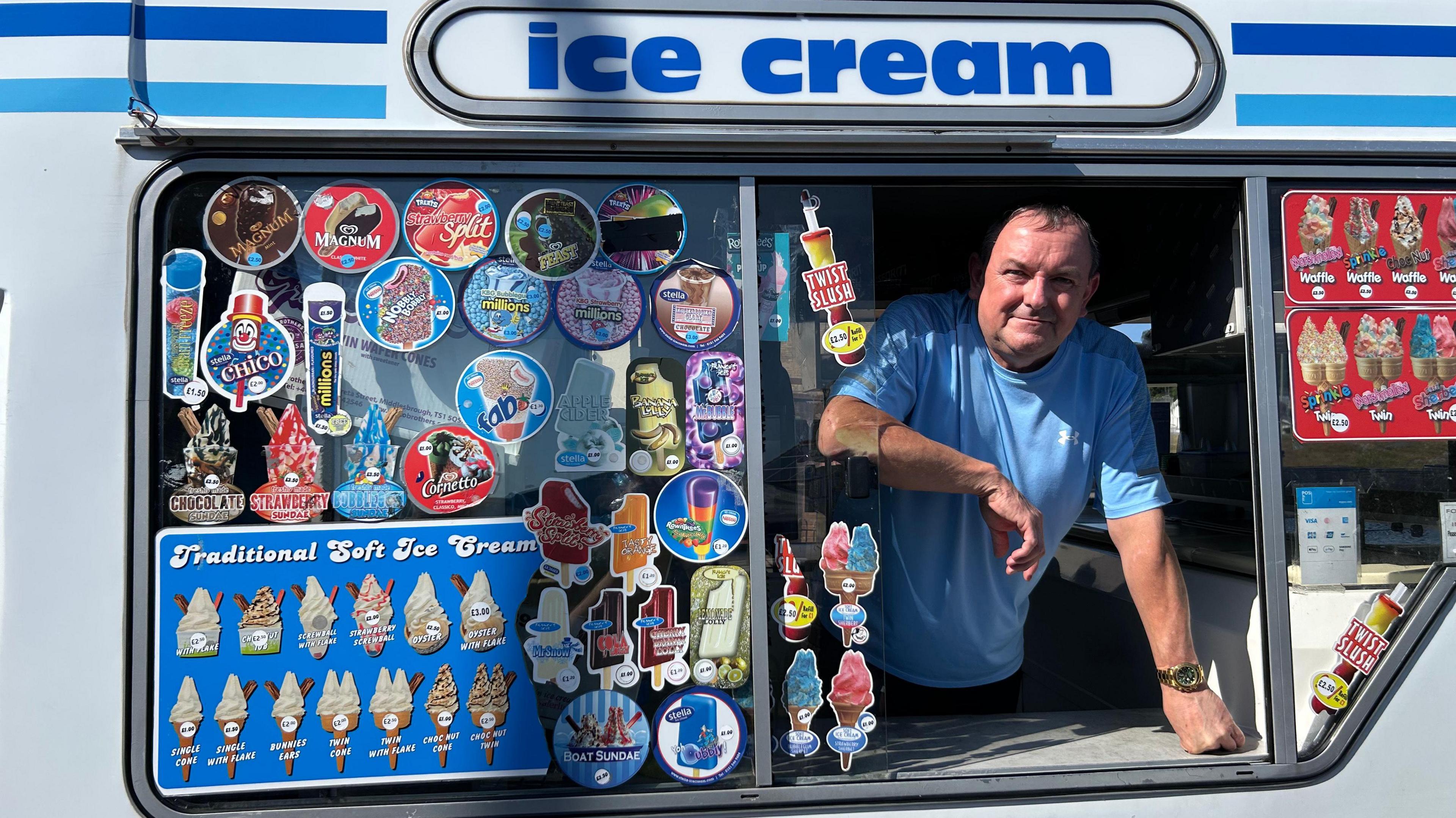 Mark Edwards looking out of the window of his ice cream van. He is wearing a blue t shirt and is looking at the camera.
