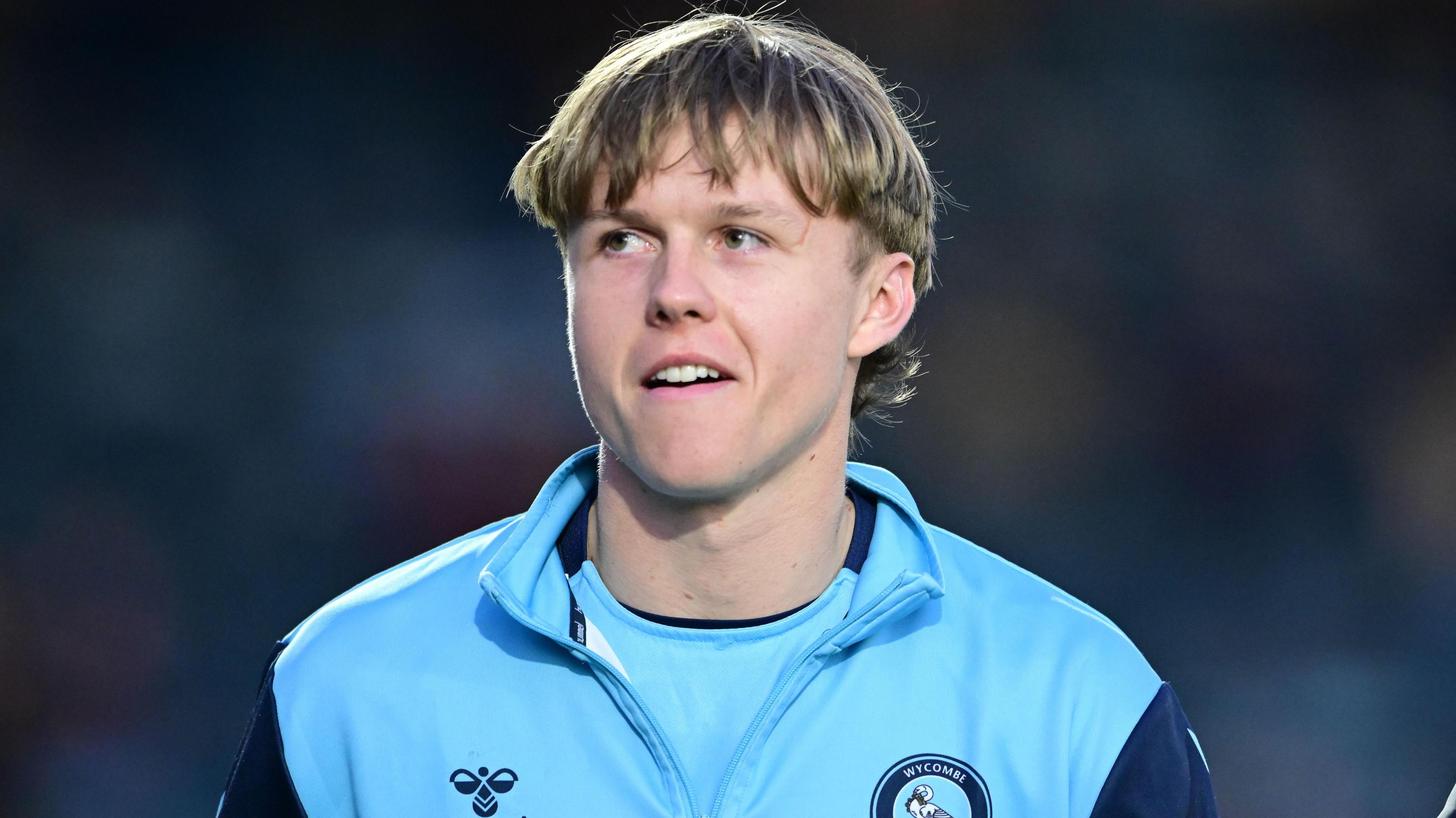 James Berry, looking to his right and smiling, while wearing a Wycombe Wanderers tracksuit